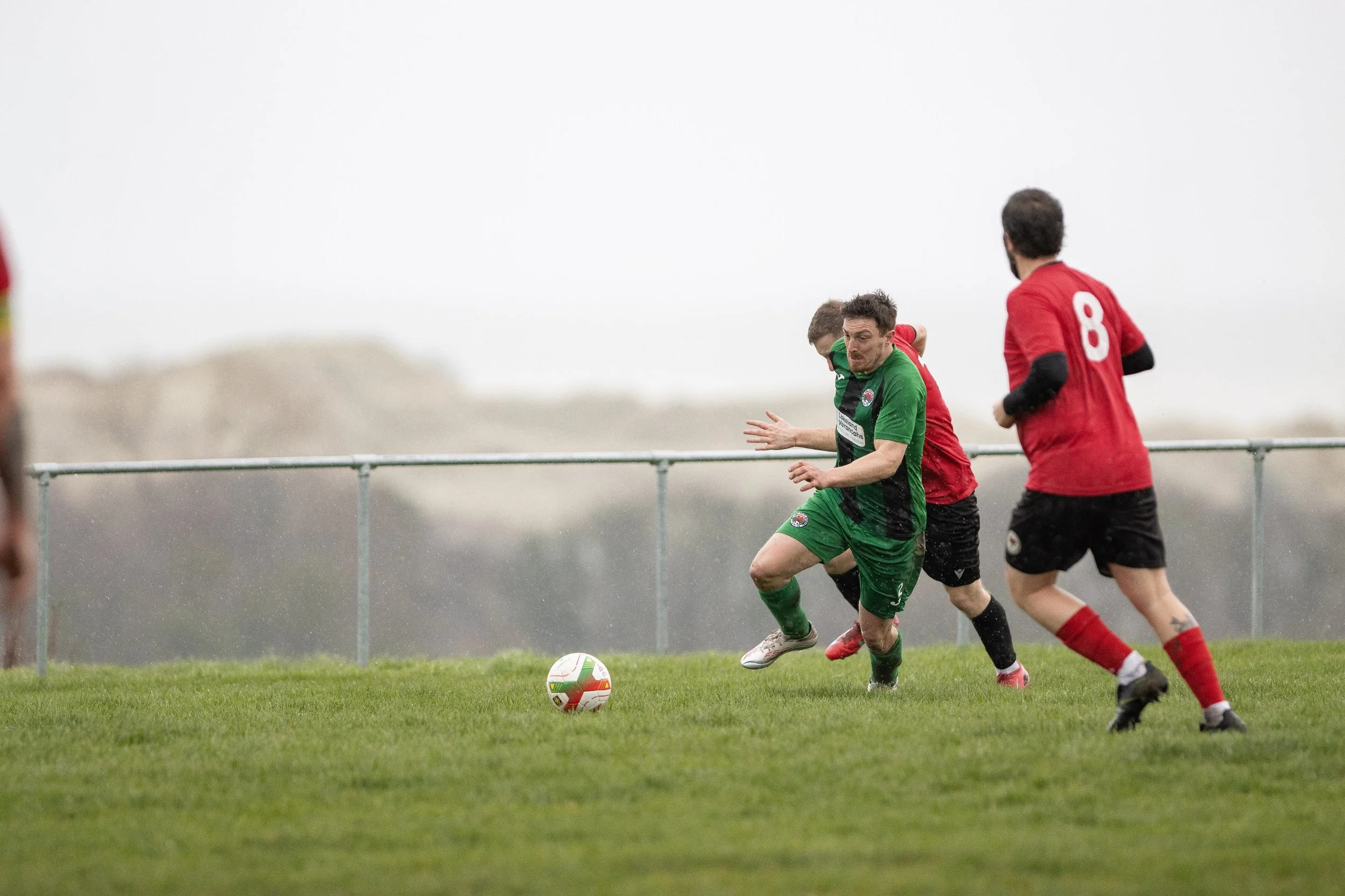 Soccer players competing for ball on grassy field under cloudy sky