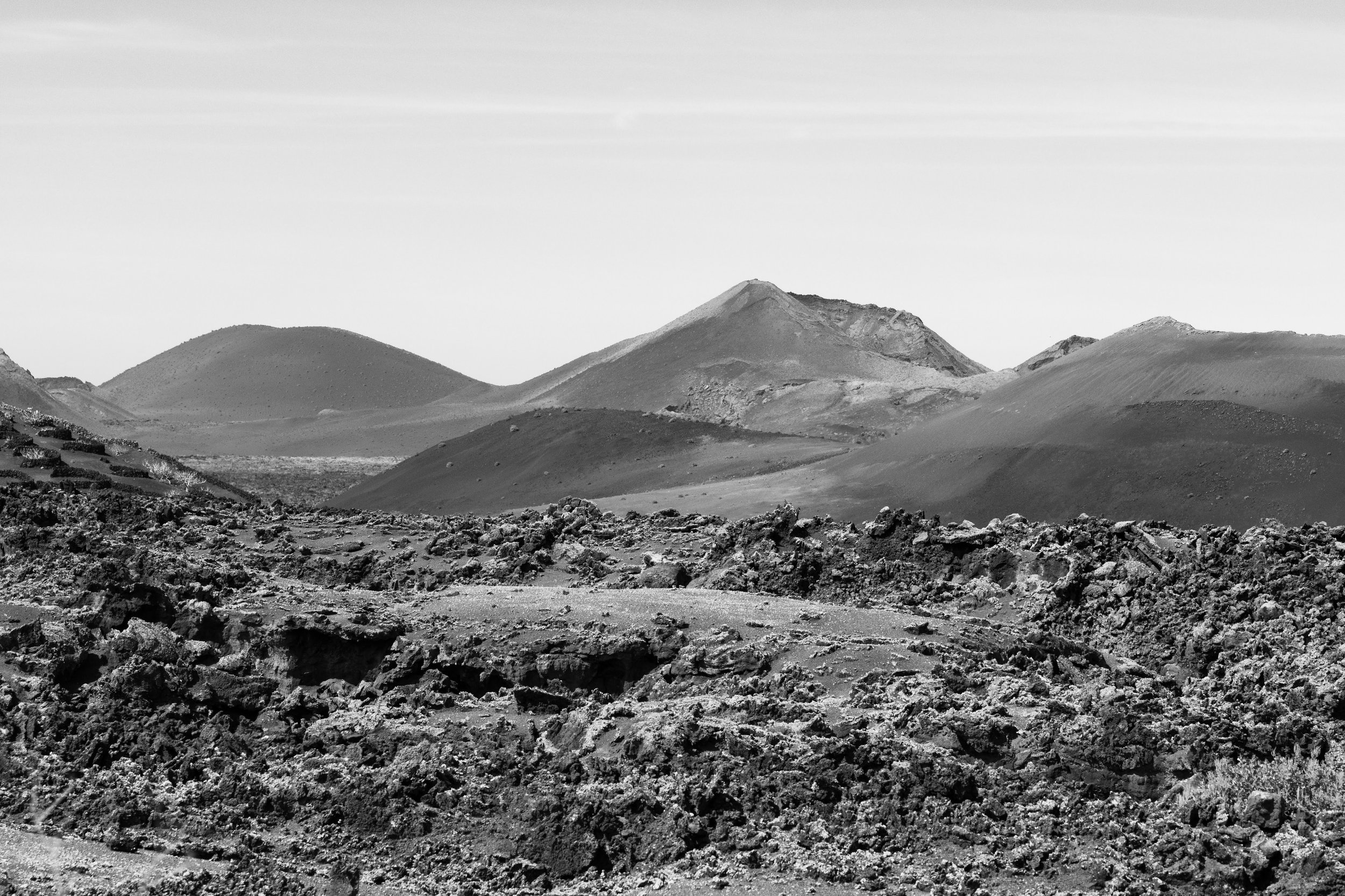 Black and white photo of volcanic landscape with rough, rocky foreground and smooth, rolling hills in the background.