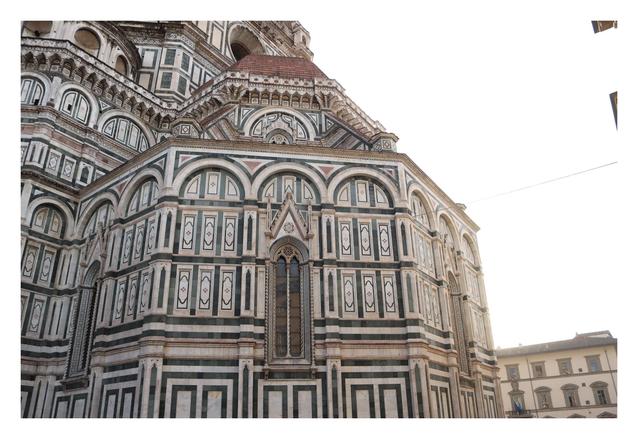 Close-up view of the intricate marble facade of the Florence Cathedral, emphasizing its detailed geometric patterns and arched windows, with a section of the building's dome visible at the top.