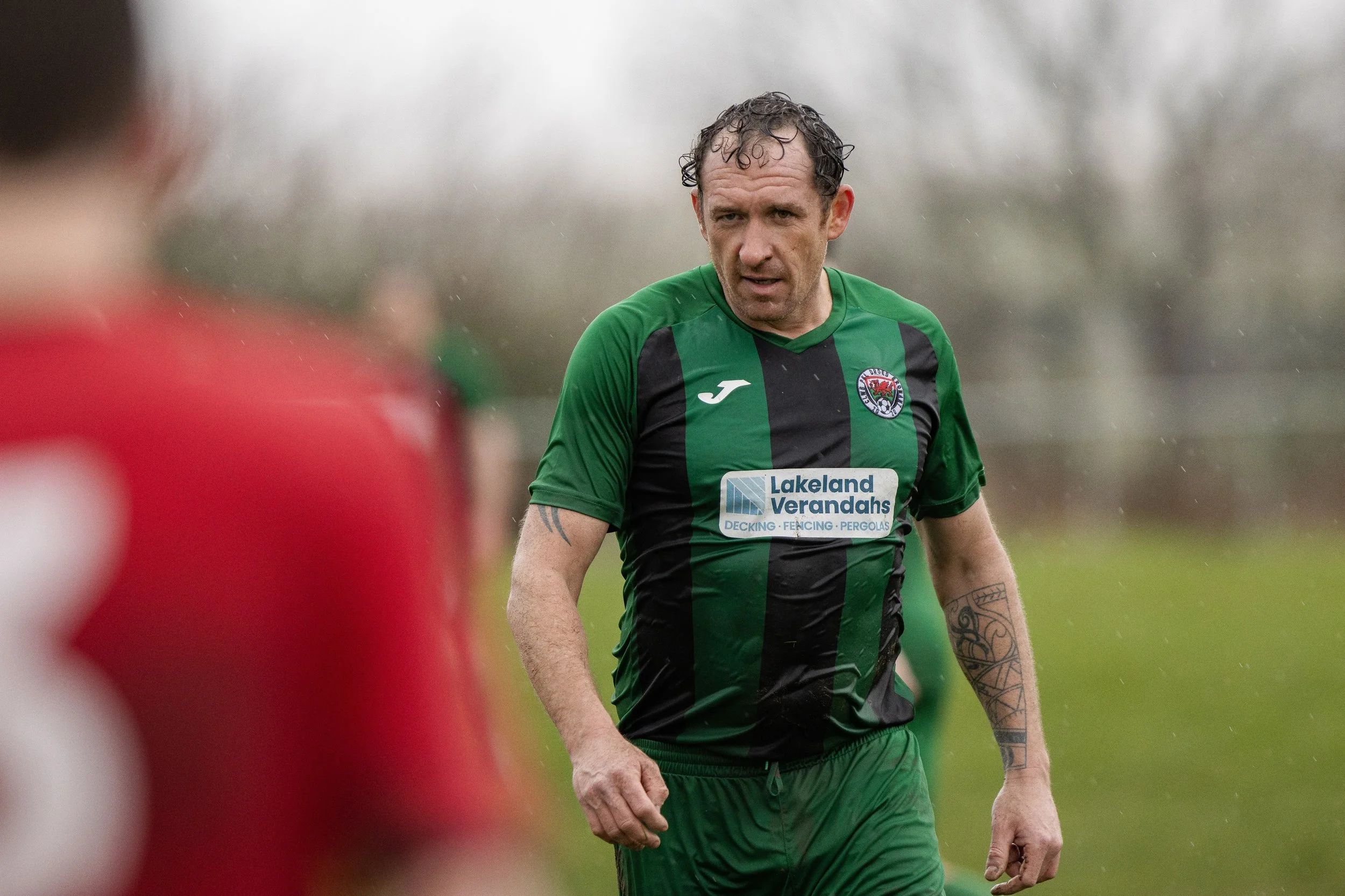 Soccer player in green and black jersey with tattoos on arm, on field, during game.
