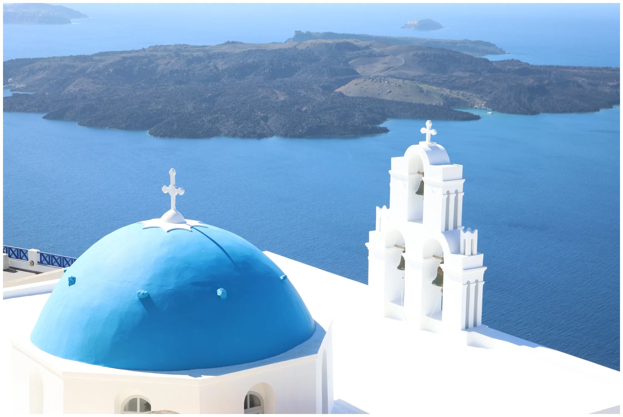 White church with blue dome and bell tower overlooking the sea in Santorini, Greece.