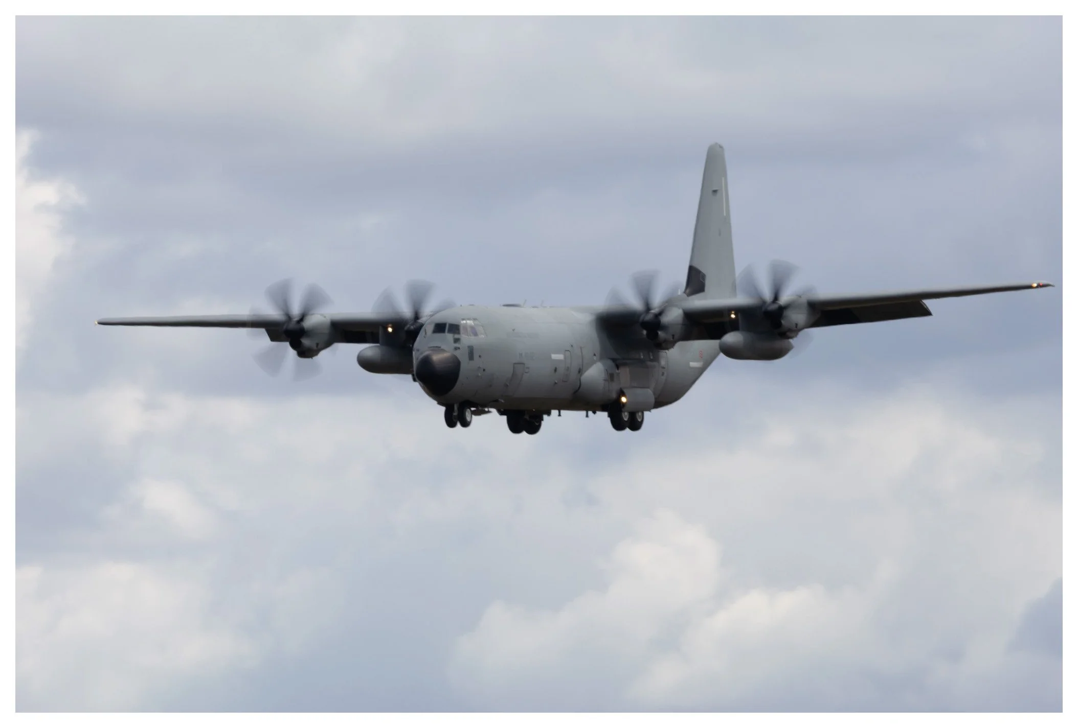 Military cargo plane flying in cloudy sky, propellers spinning.
