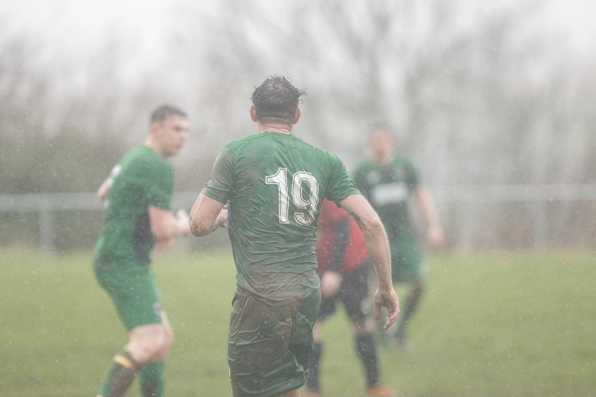 Soccer players in rain during a game, focusing on player wearing jersey number 19.