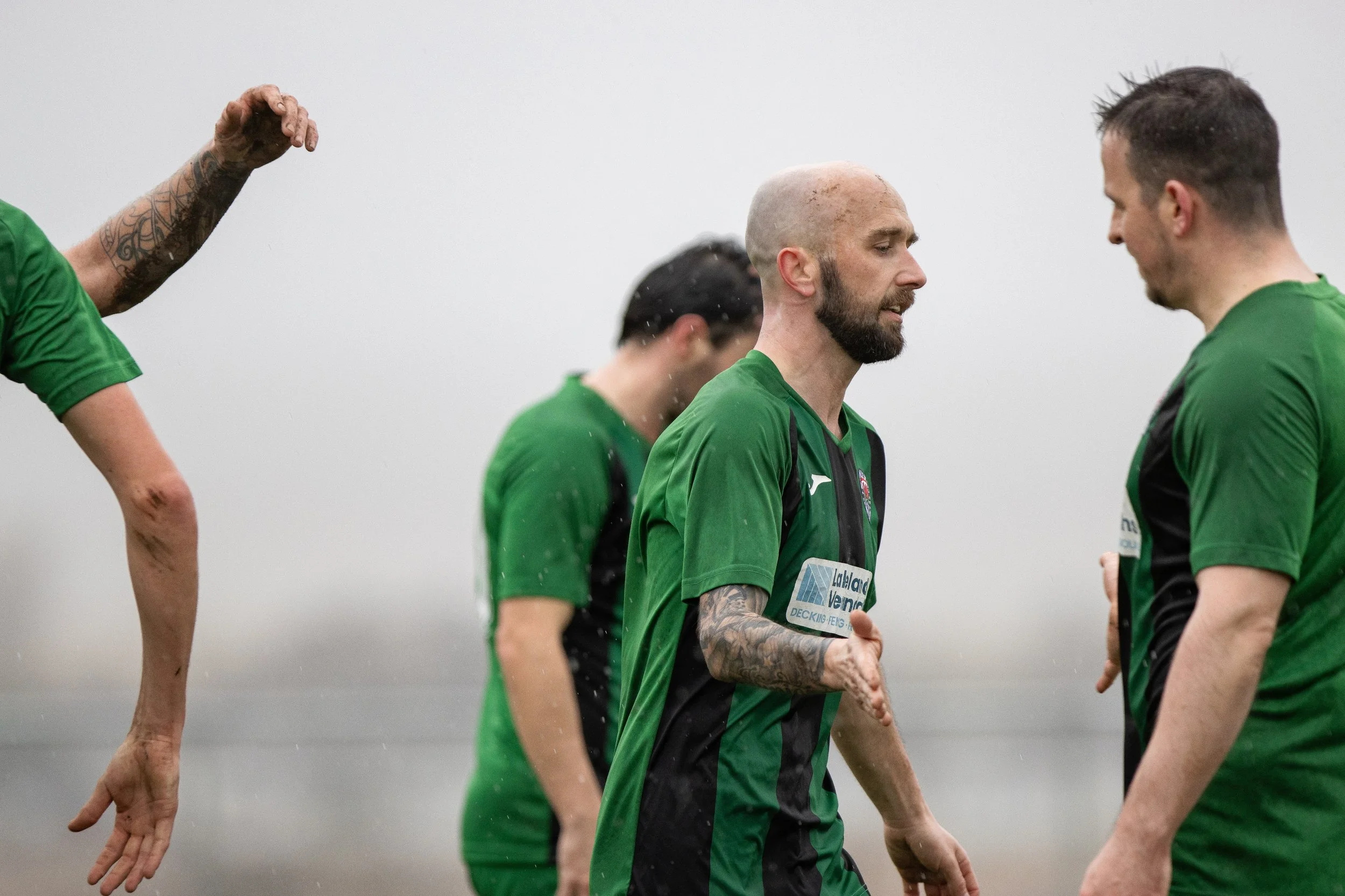 Soccer players in green jerseys on field in rainy weather, greeting each other with handshakes.