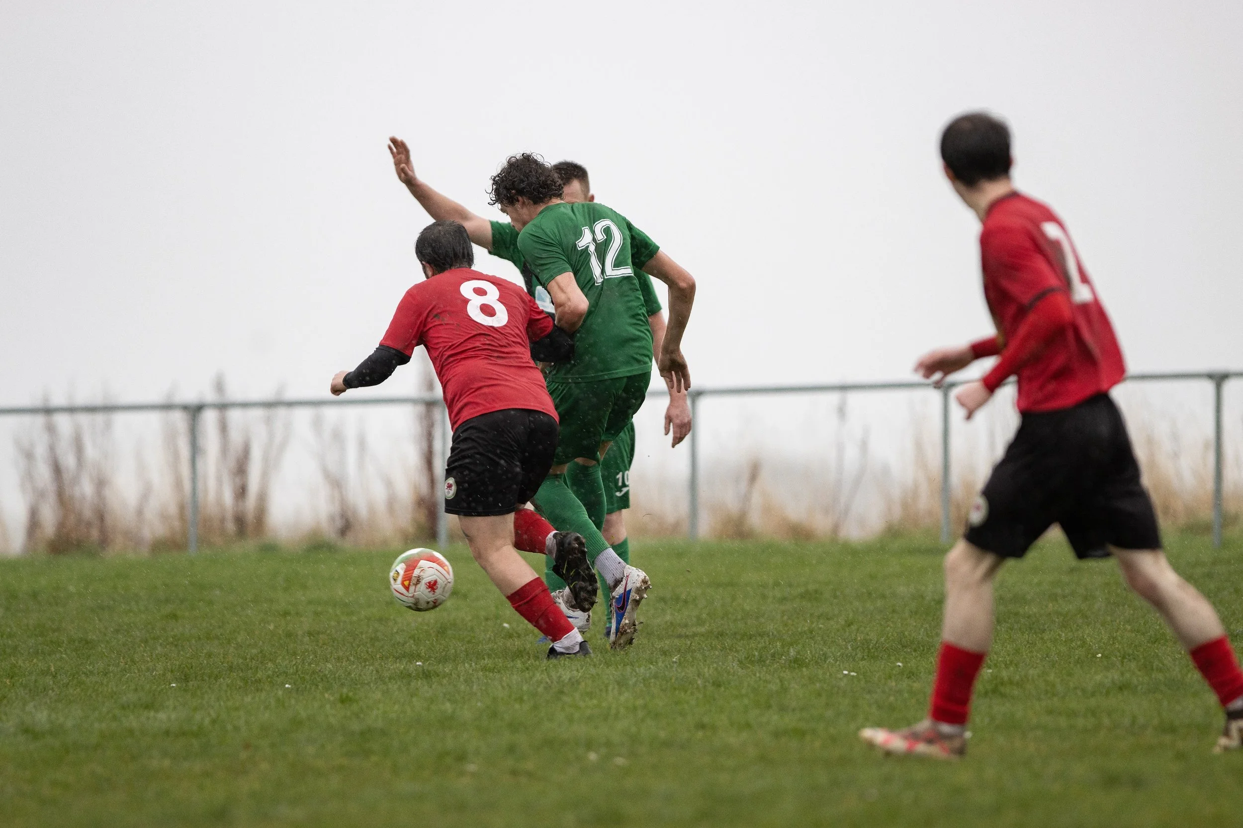 Soccer players in red and green uniforms competing for the ball on a grassy field during a match.