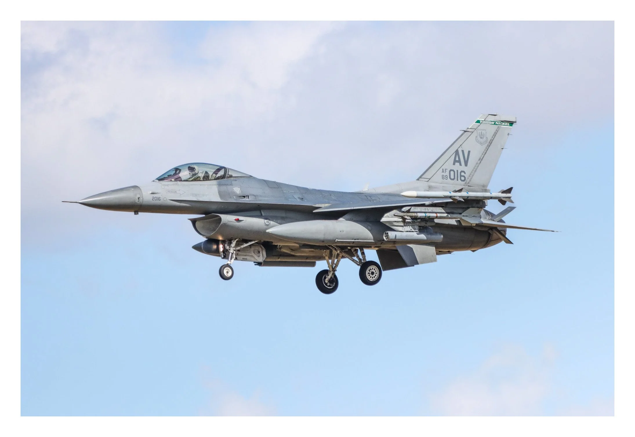 A military fighter jet flying in the sky with a mostly blue background and some clouds.