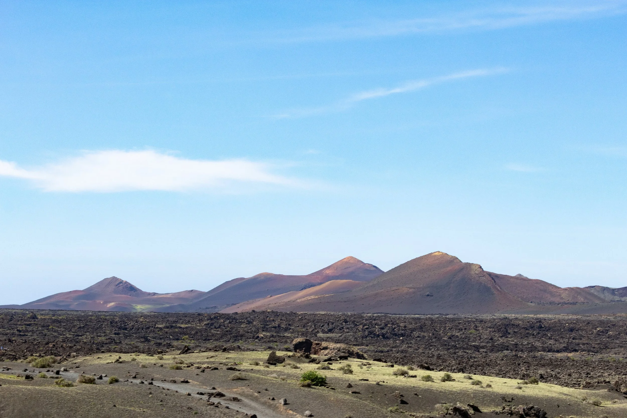 A barren, rocky desert landscape with volcanic mountains in the background under a clear blue sky.