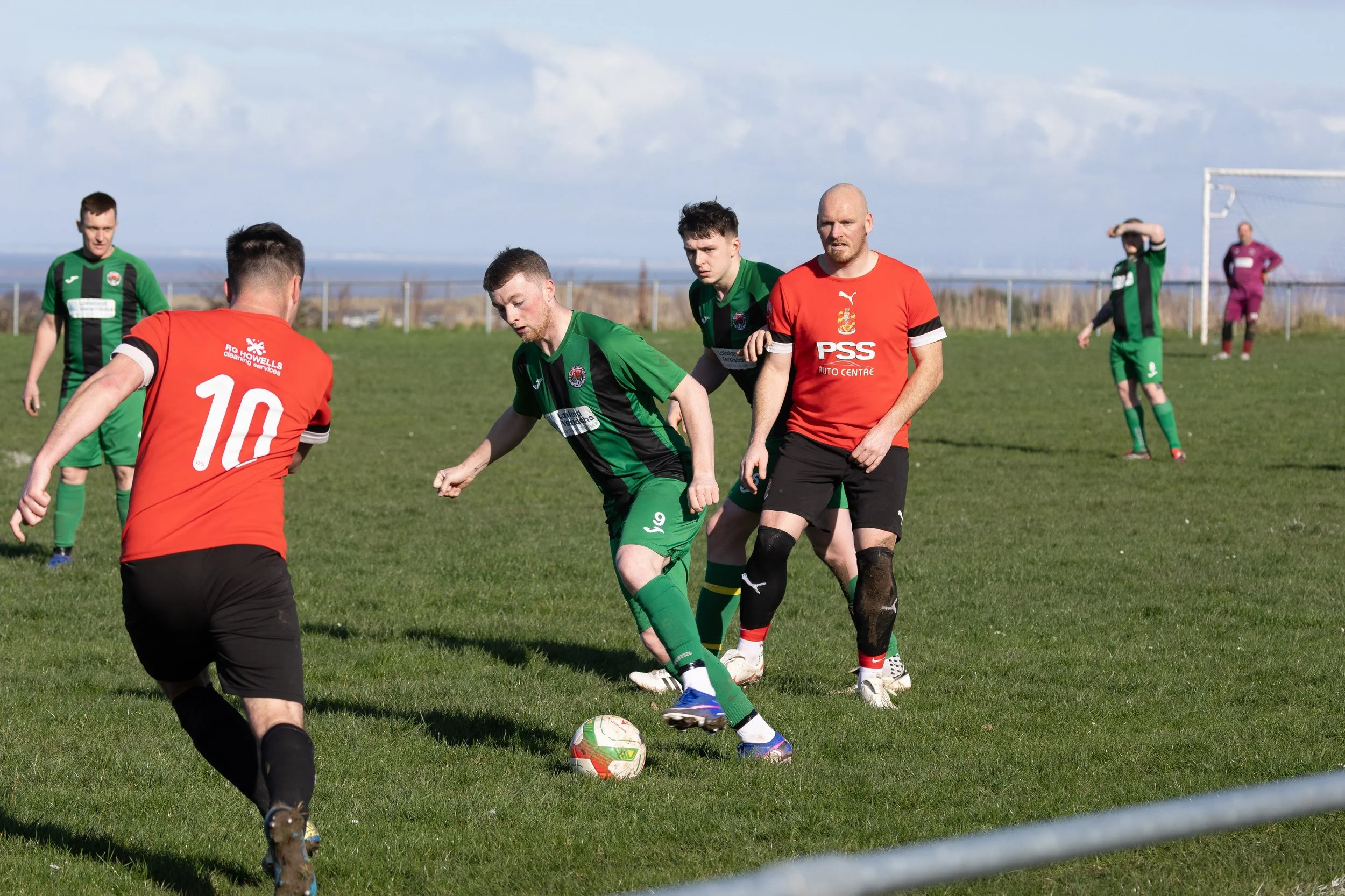 Soccer players on the field during a game, green and red team uniforms, one player in red with number 10, green team player dribbling the ball.