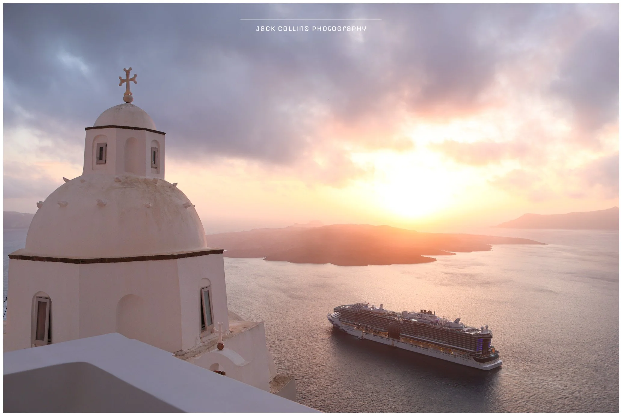 A white church with a dome and cross in Santorini, Greece, overlooking the sea with a cruise ship at sunset.