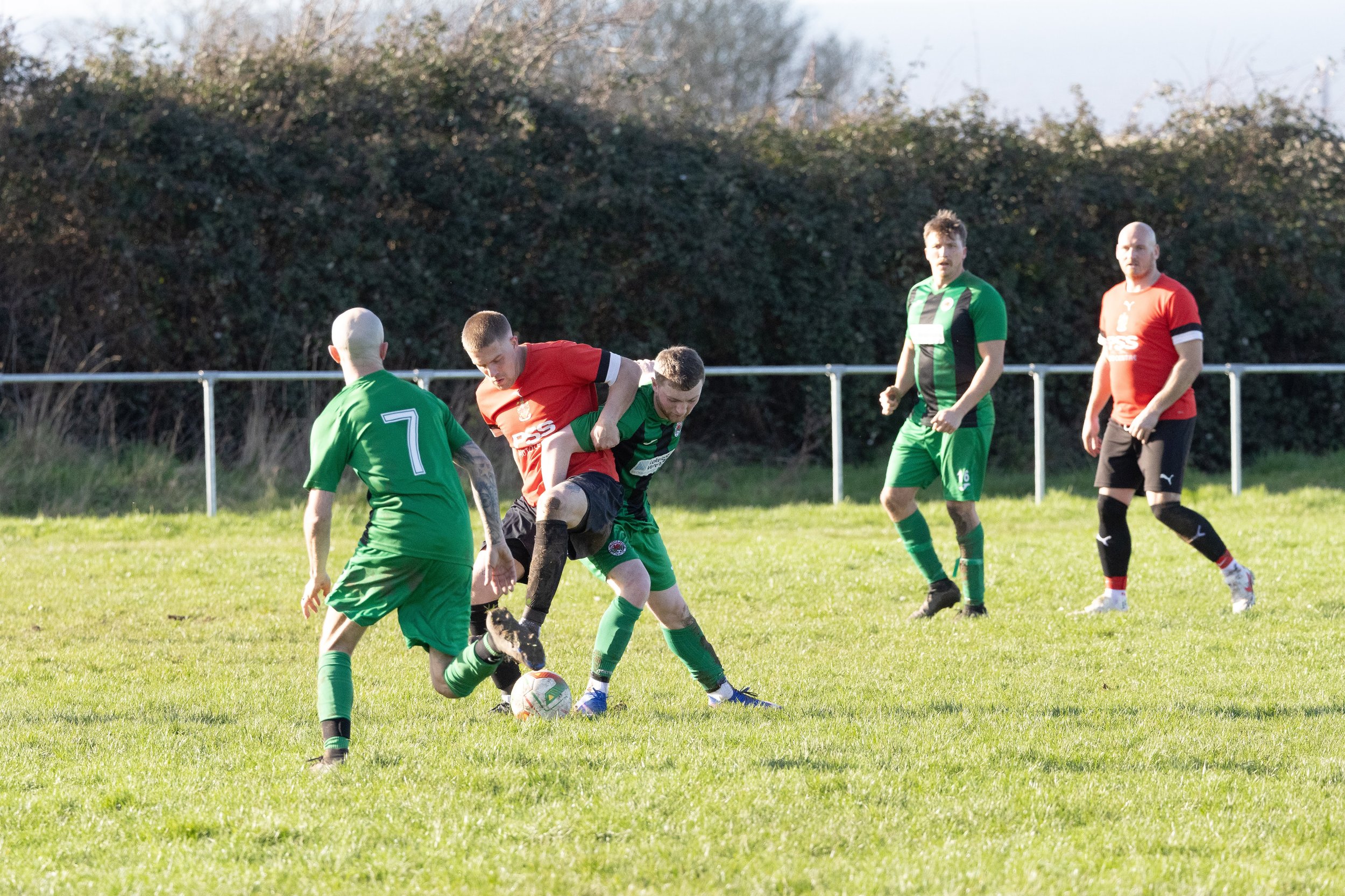 Soccer players in green and red uniforms competing for the ball on a grassy field.