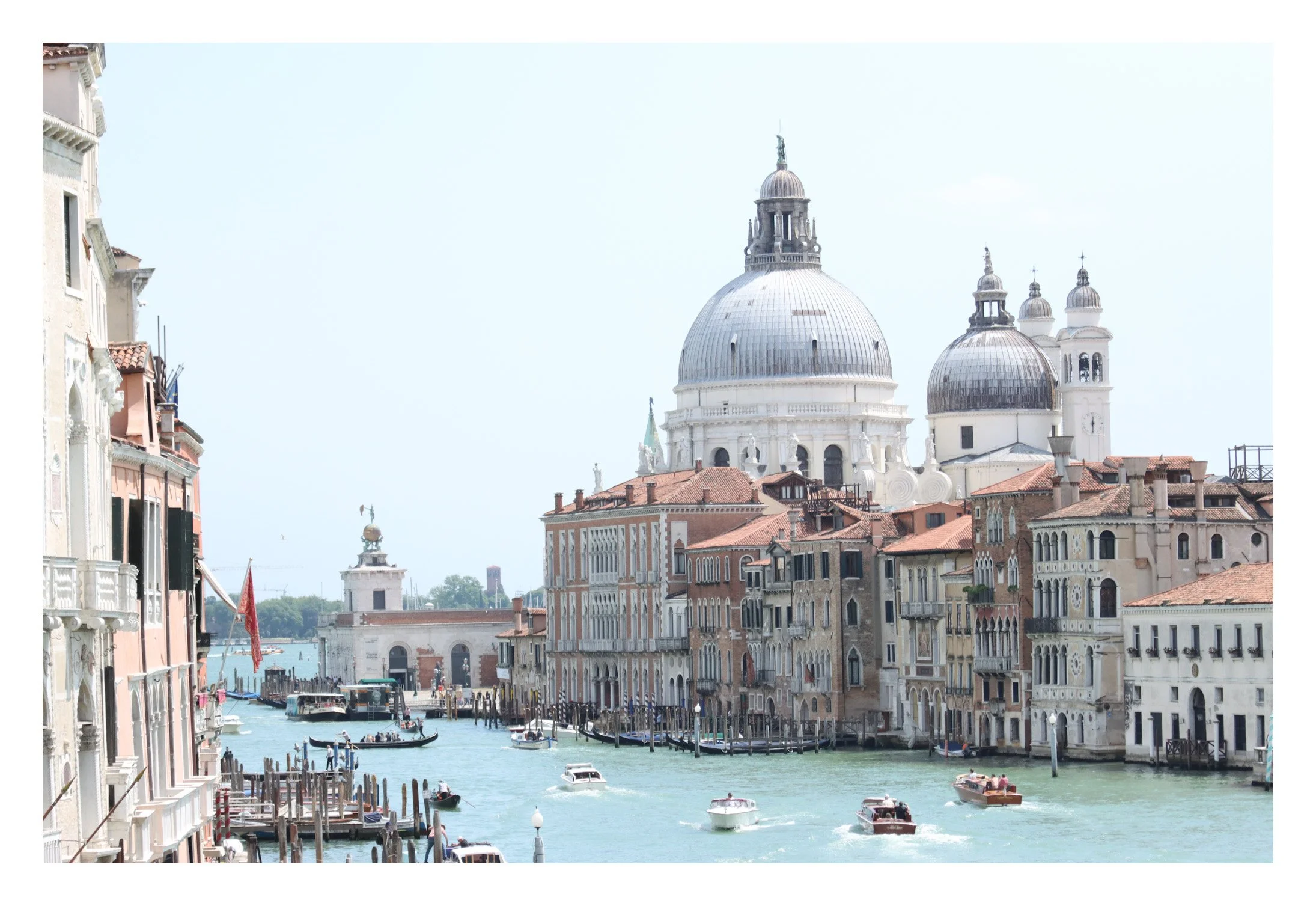 Venetian canal with boats and historic buildings along water, featuring prominent domed church in the background.