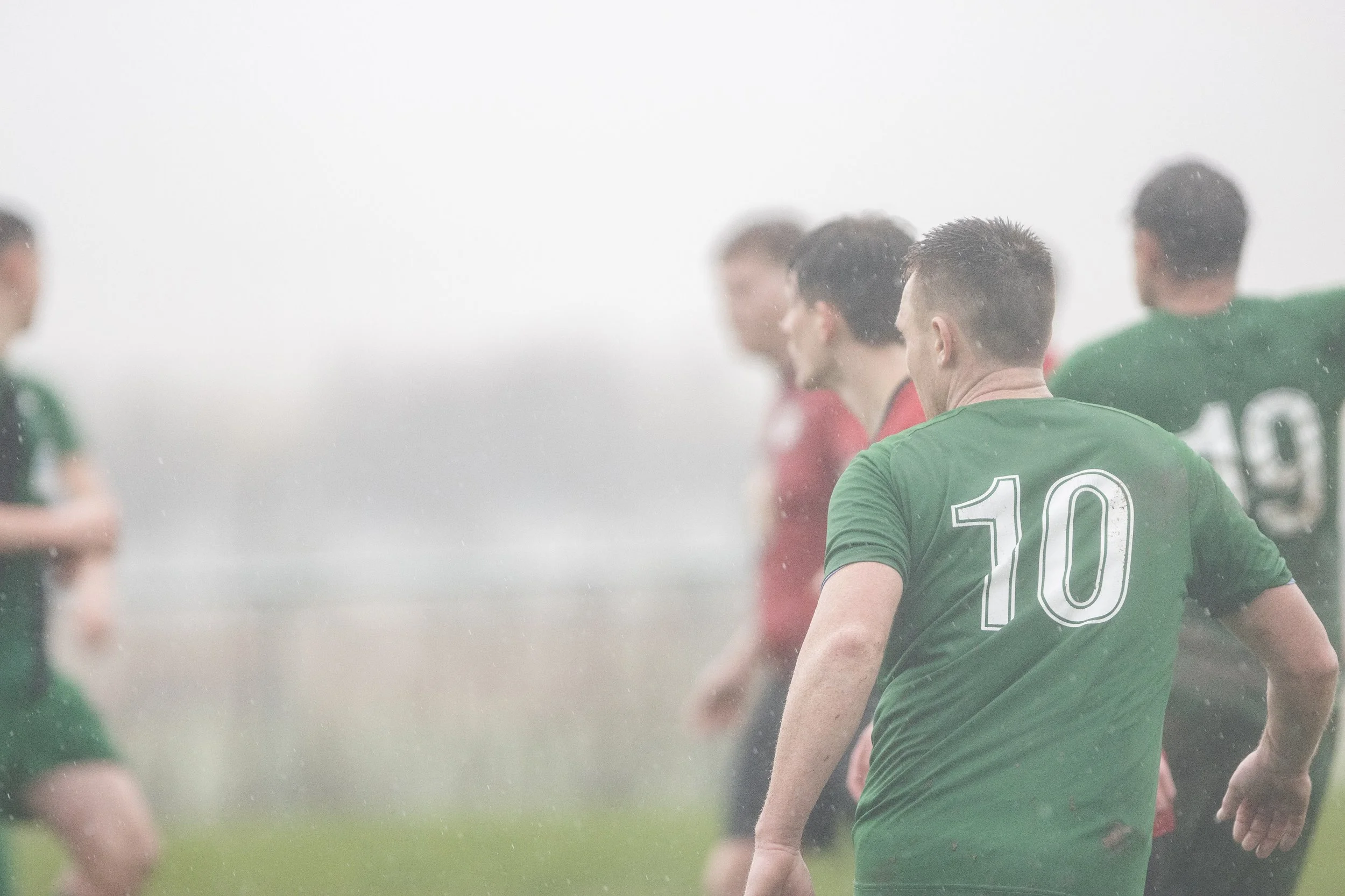 Soccer players on the field during a rainy match, wearing green and red jerseys.