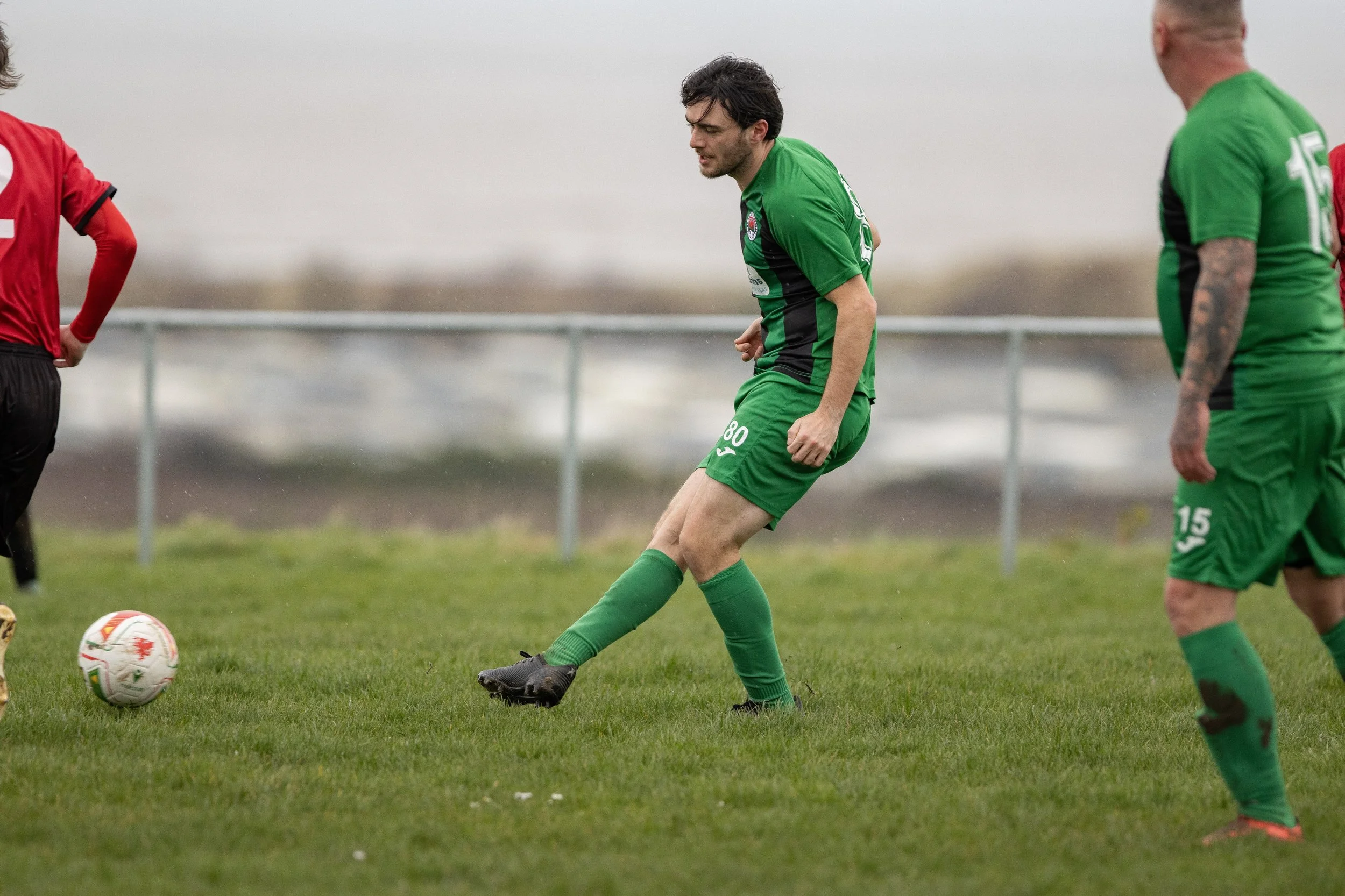 Soccer players practicing on a grassy field, with one player in a green uniform kicking the ball, and others nearby.