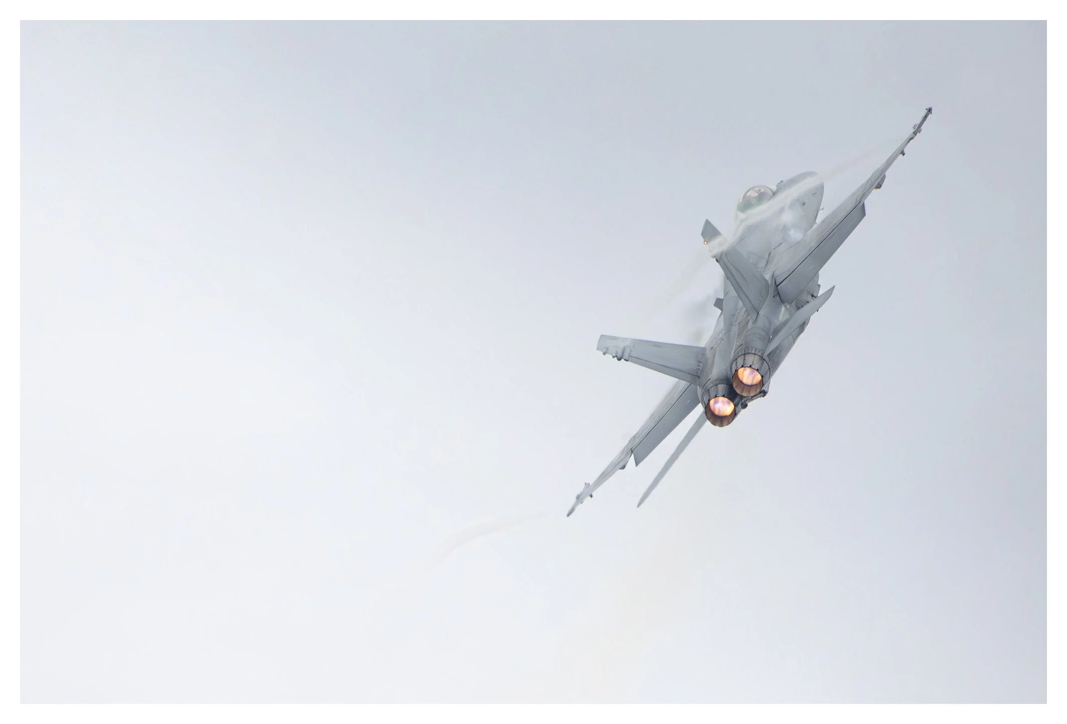 A fighter jet flying through a cloudy sky with its afterburners on.