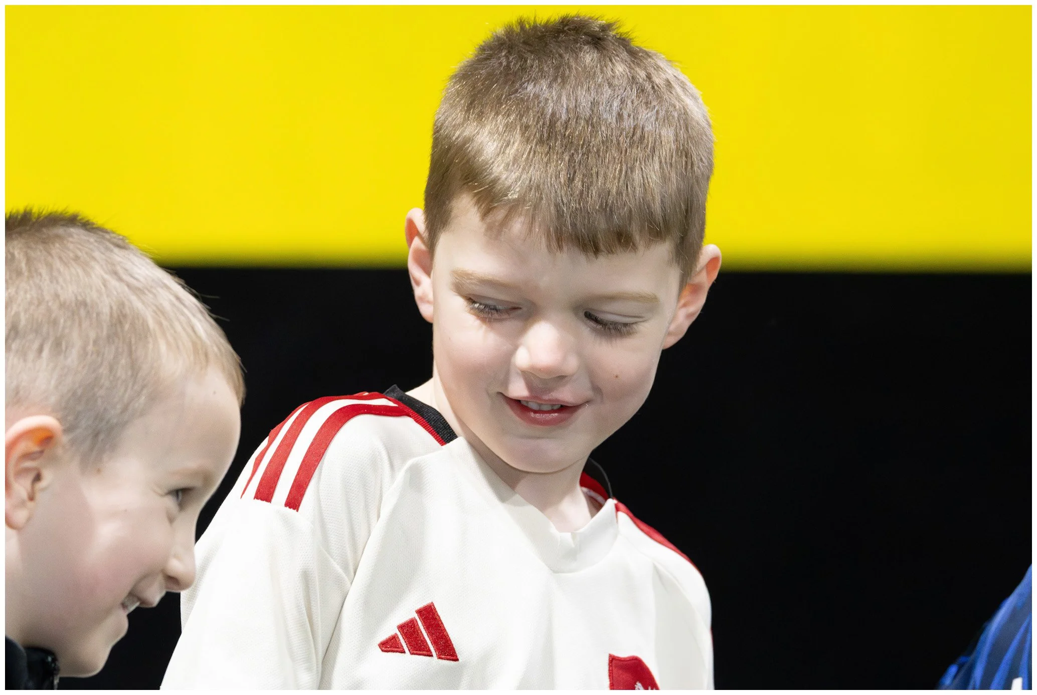 Three young boys are looking at each other and smiling, with a yellow background.