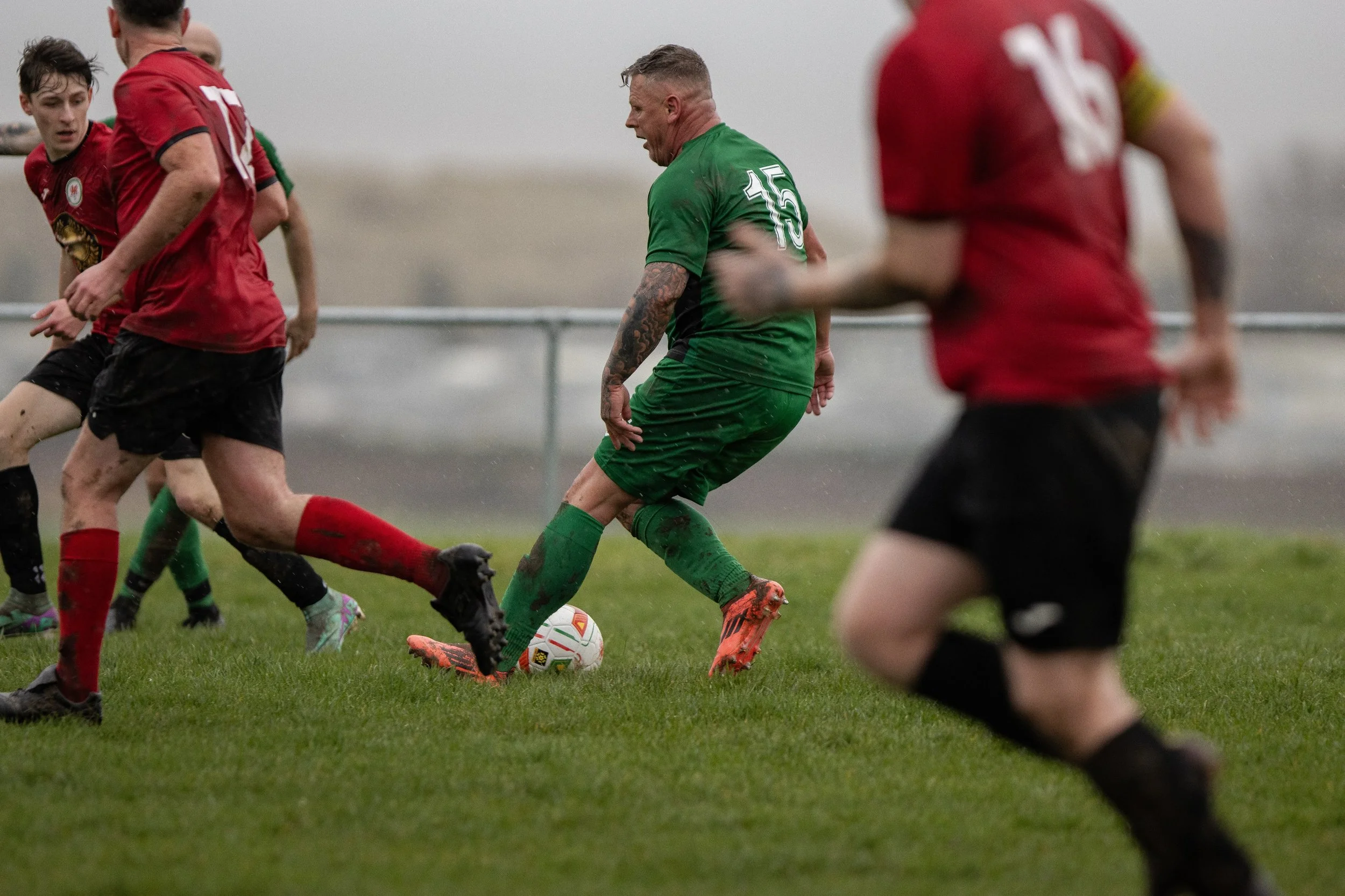 Soccer players in red and green jerseys competing for the ball on a grassy field.