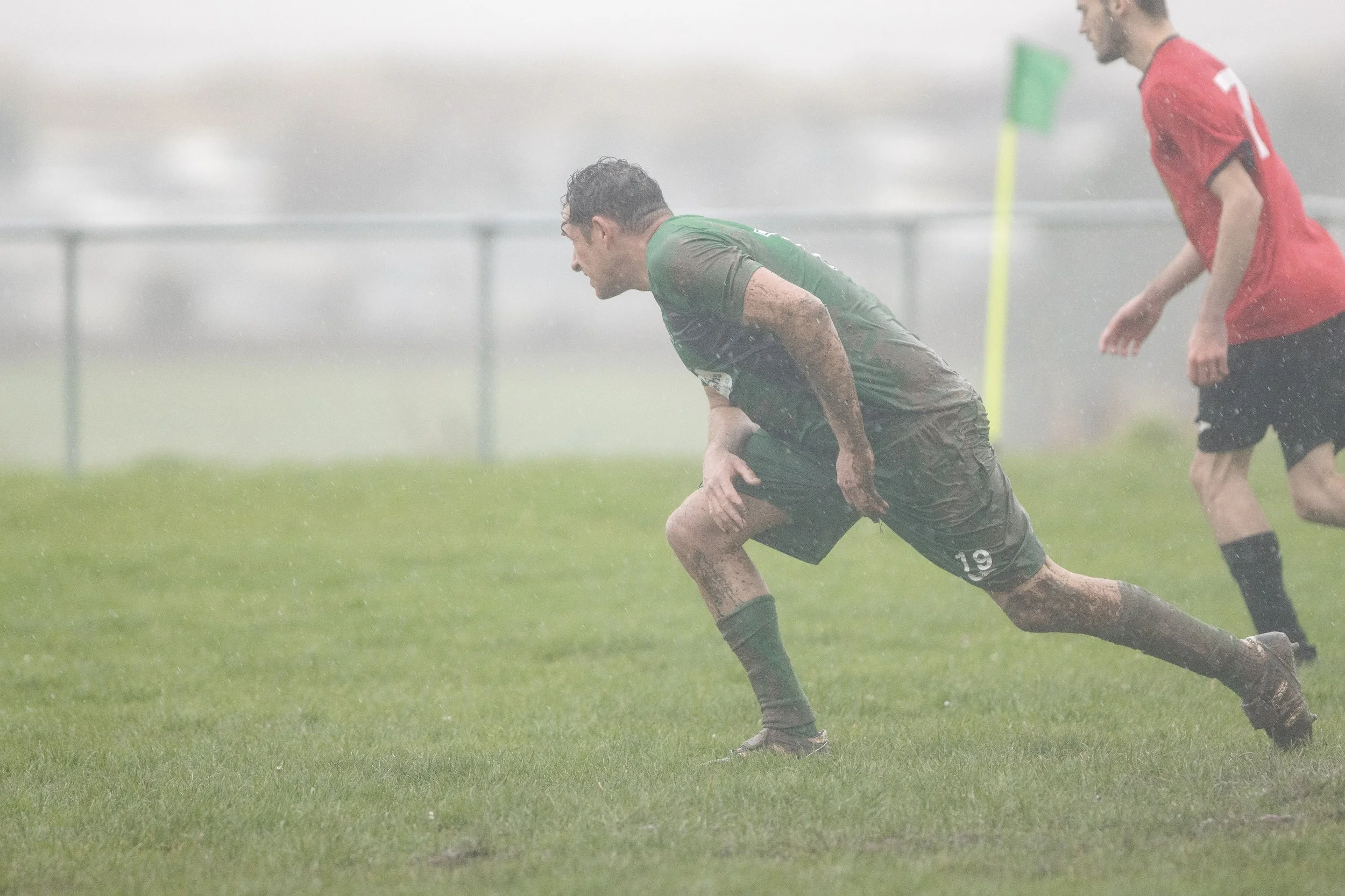Two soccer players in muddy uniforms playing in heavy rain on a grass field