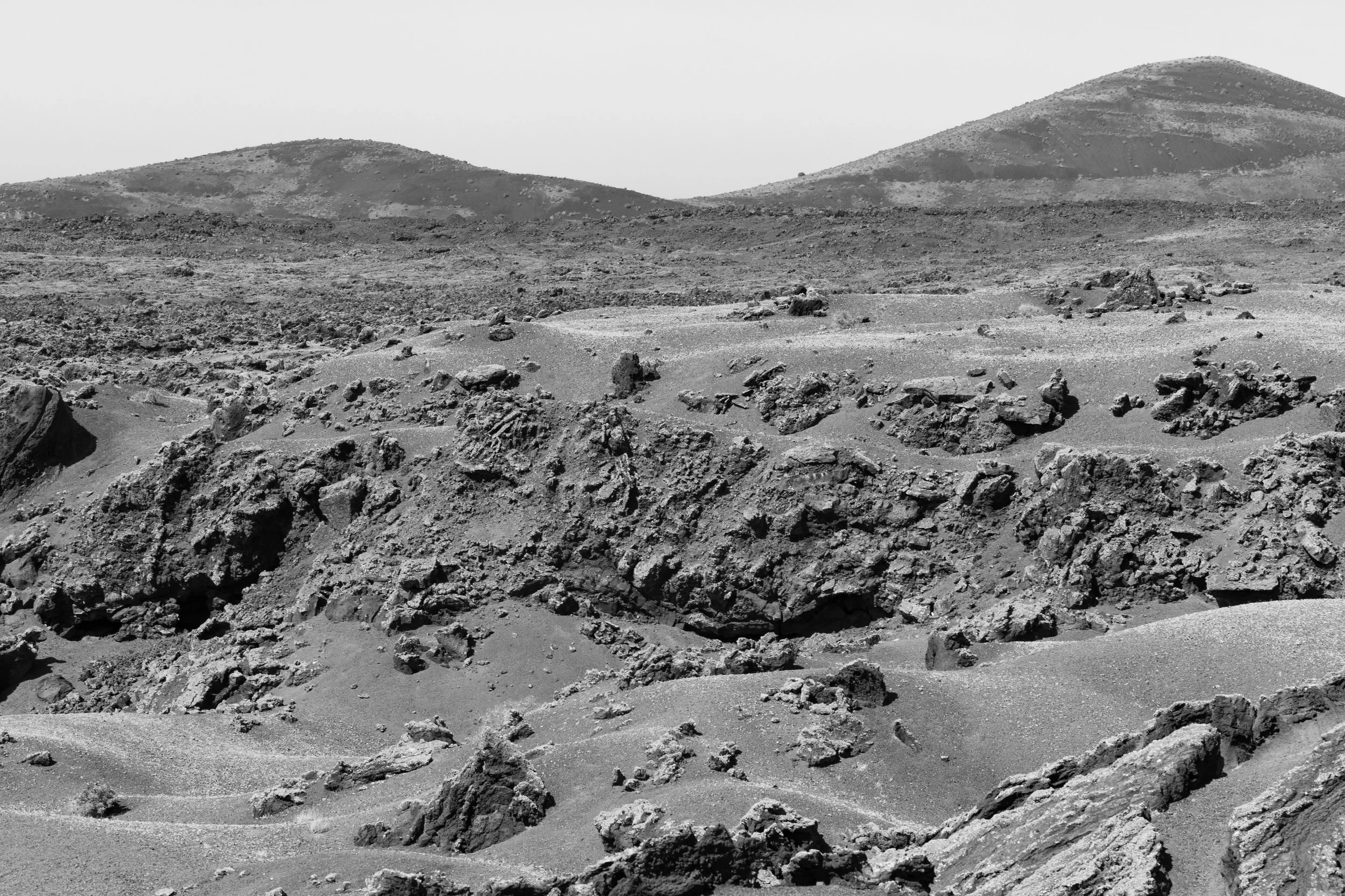 Black and white photo of a rugged, rocky desert landscape with hills in the background.