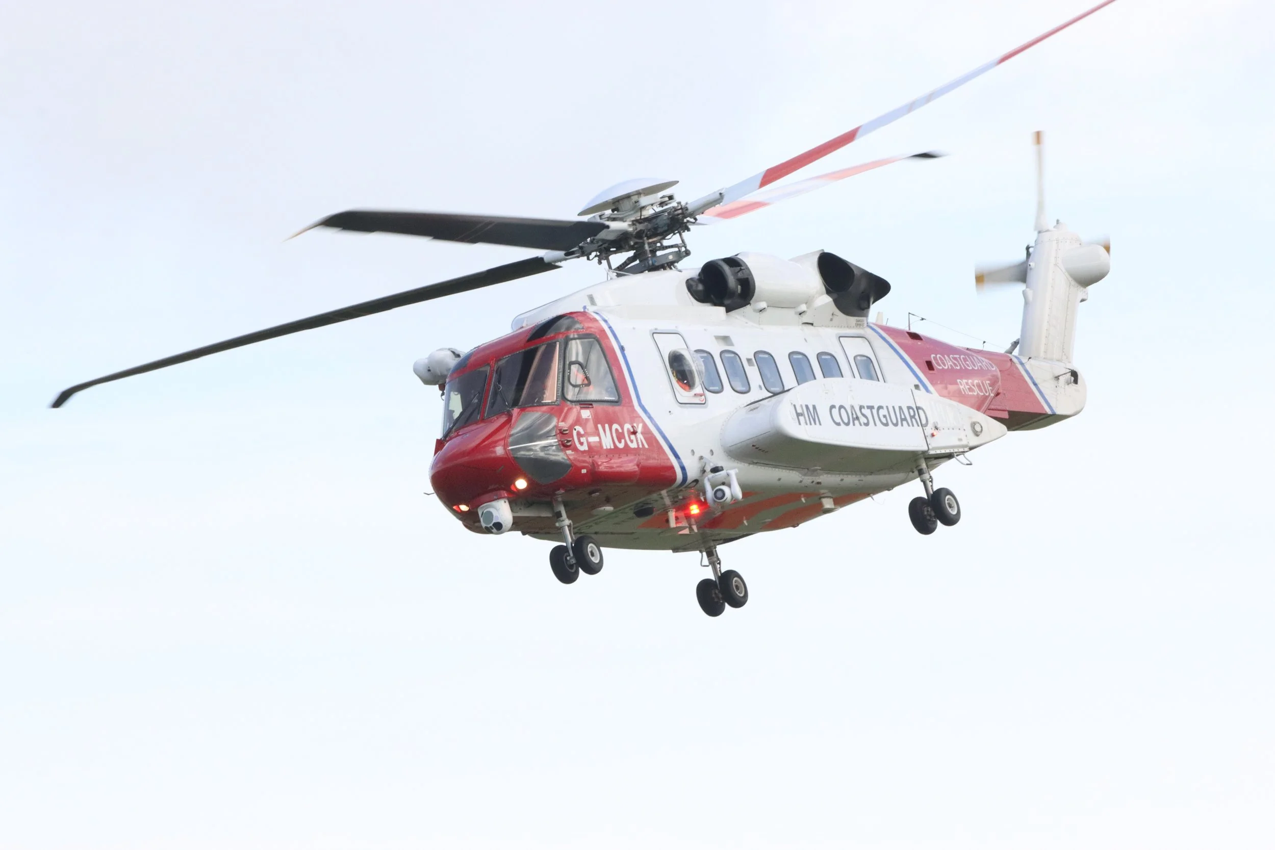 A red and white helicopter labeled 'HM COASTGUARD' flying in the sky.