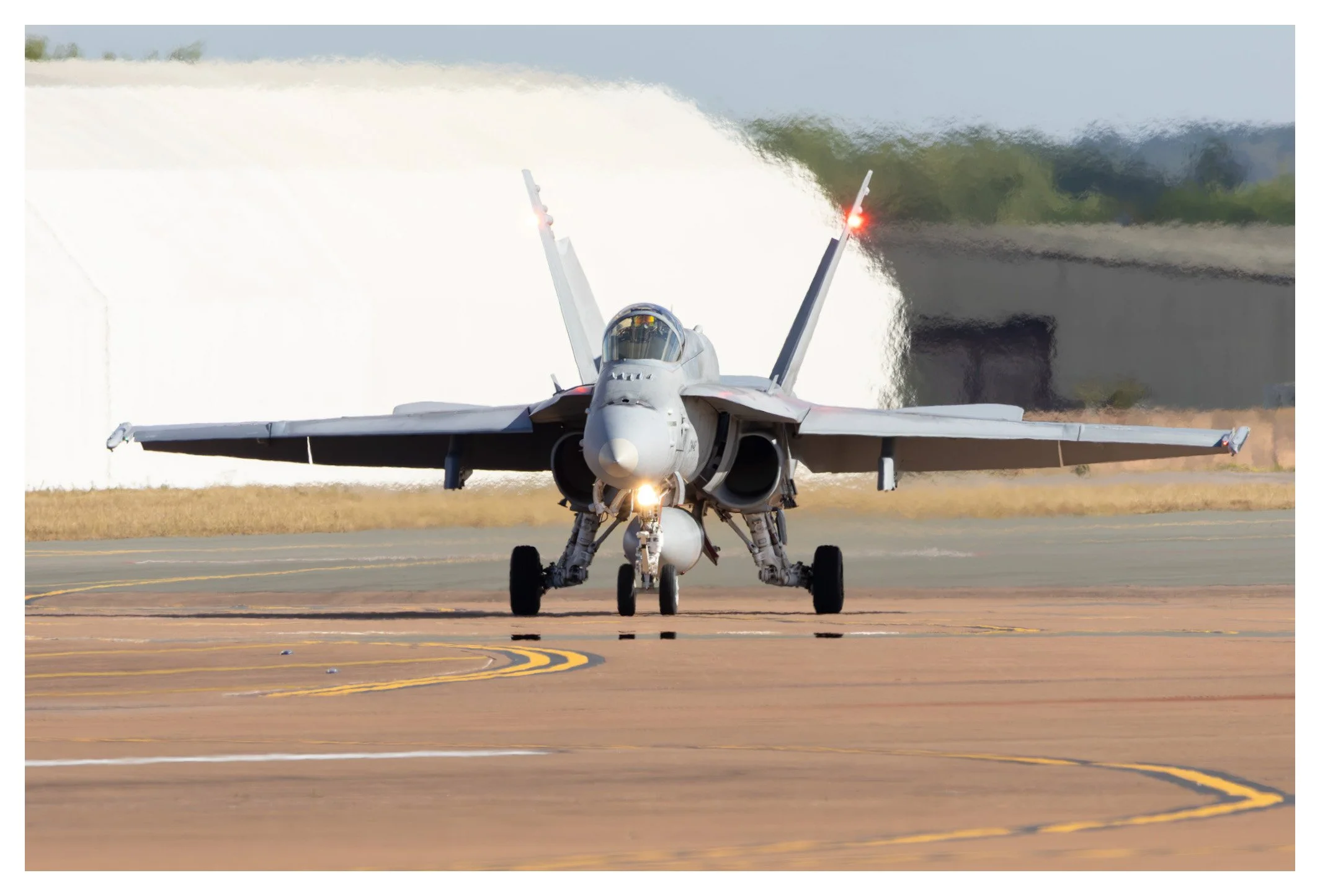 Front view of a gray fighter jet taxiing on a runway, with a water spray in the background.