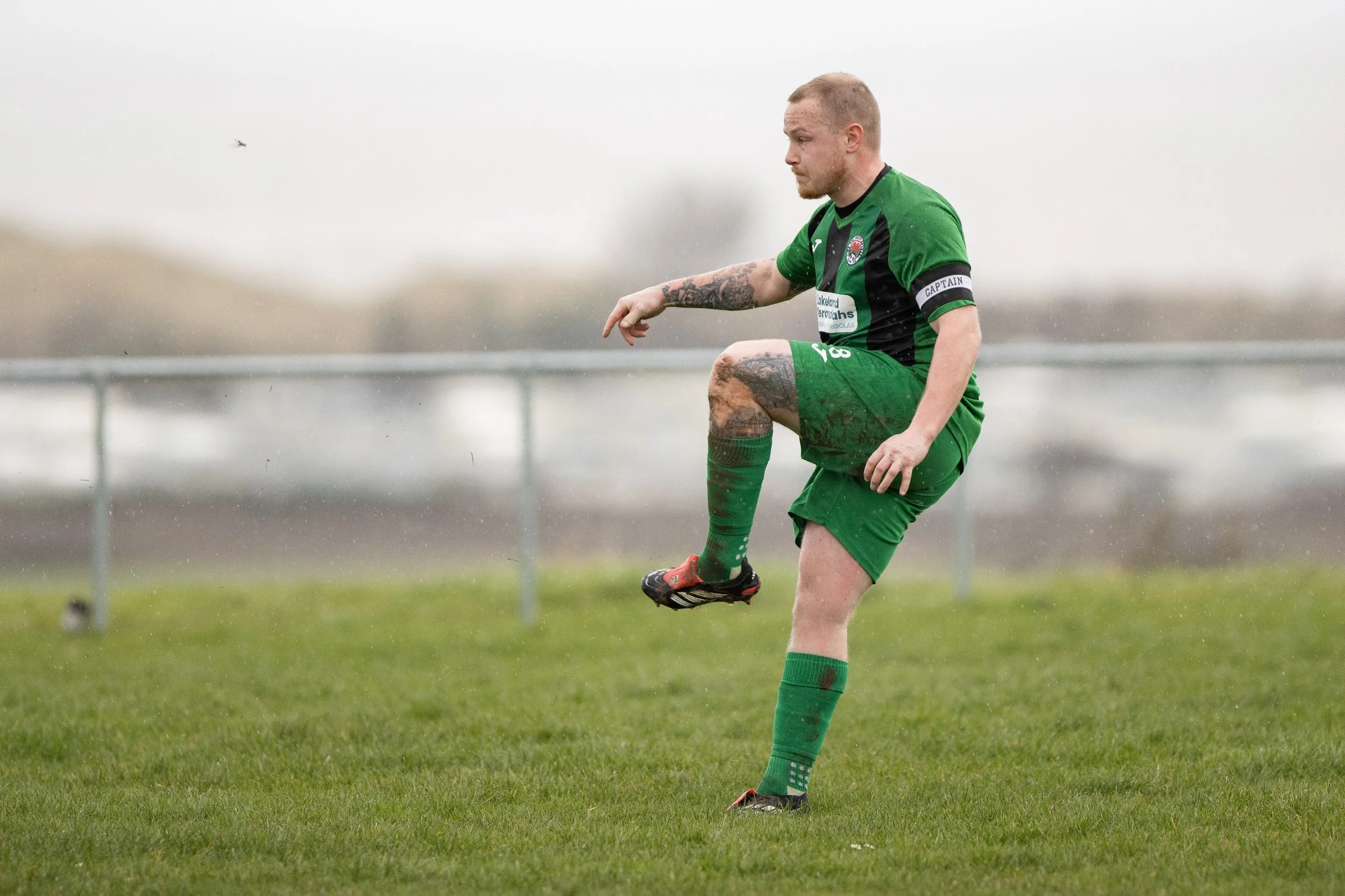 Soccer player in green uniform practicing on muddy field