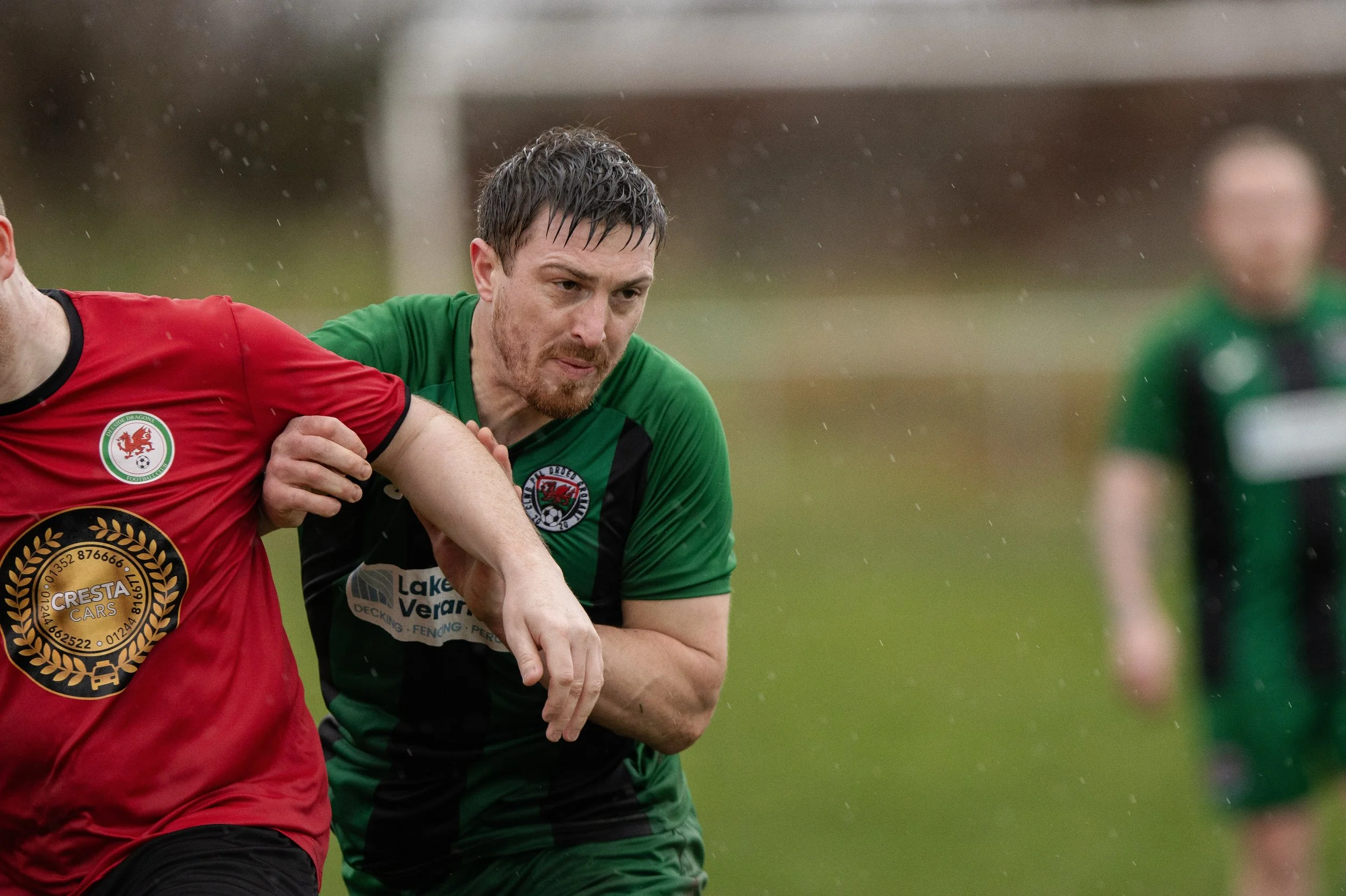 A soccer match with players in red and green jerseys playing outdoors in the rain.