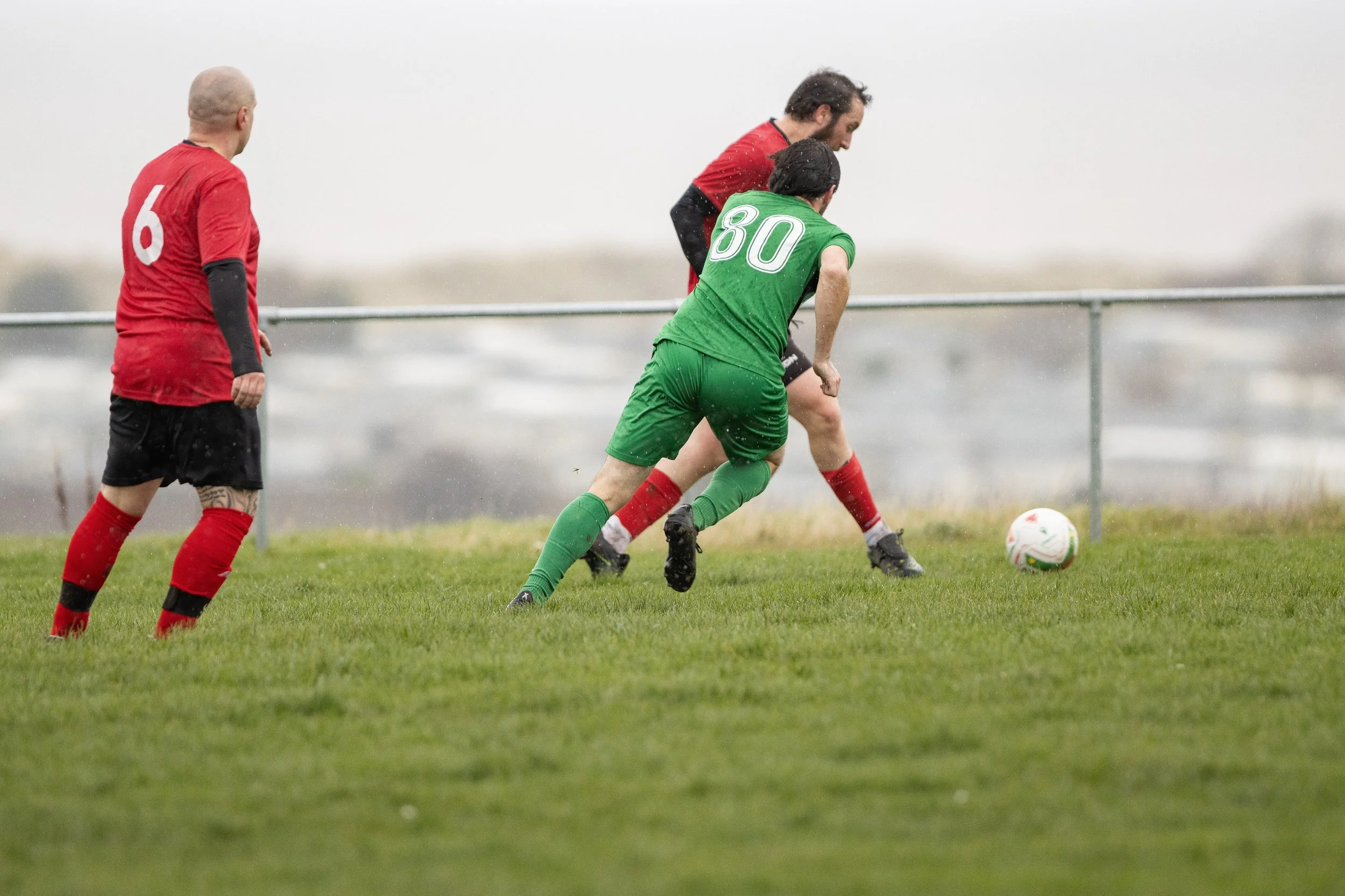 Soccer players competing for the ball on the field during a match, with players wearing red and green uniforms.
