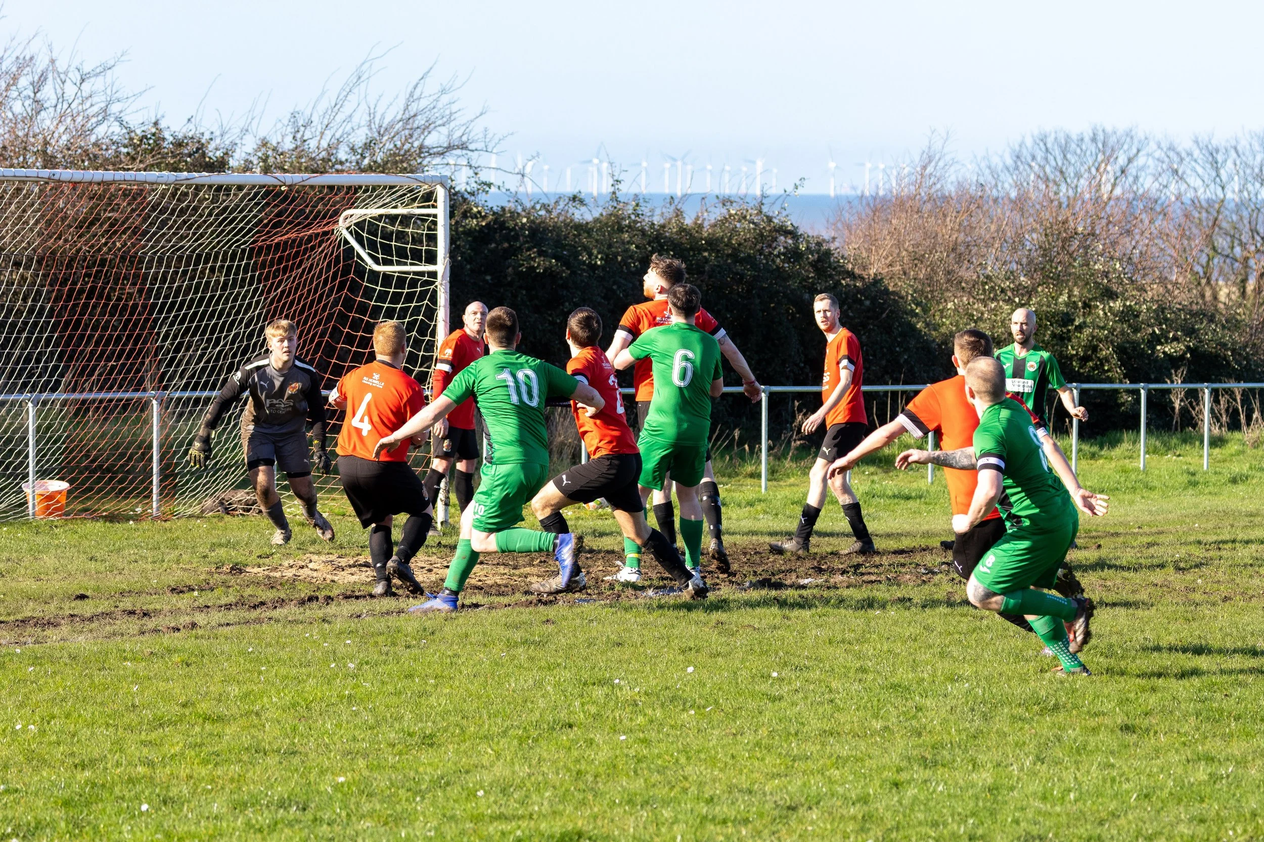 Soccer game with players competing for the ball near the goal on a grassy field under clear skies.