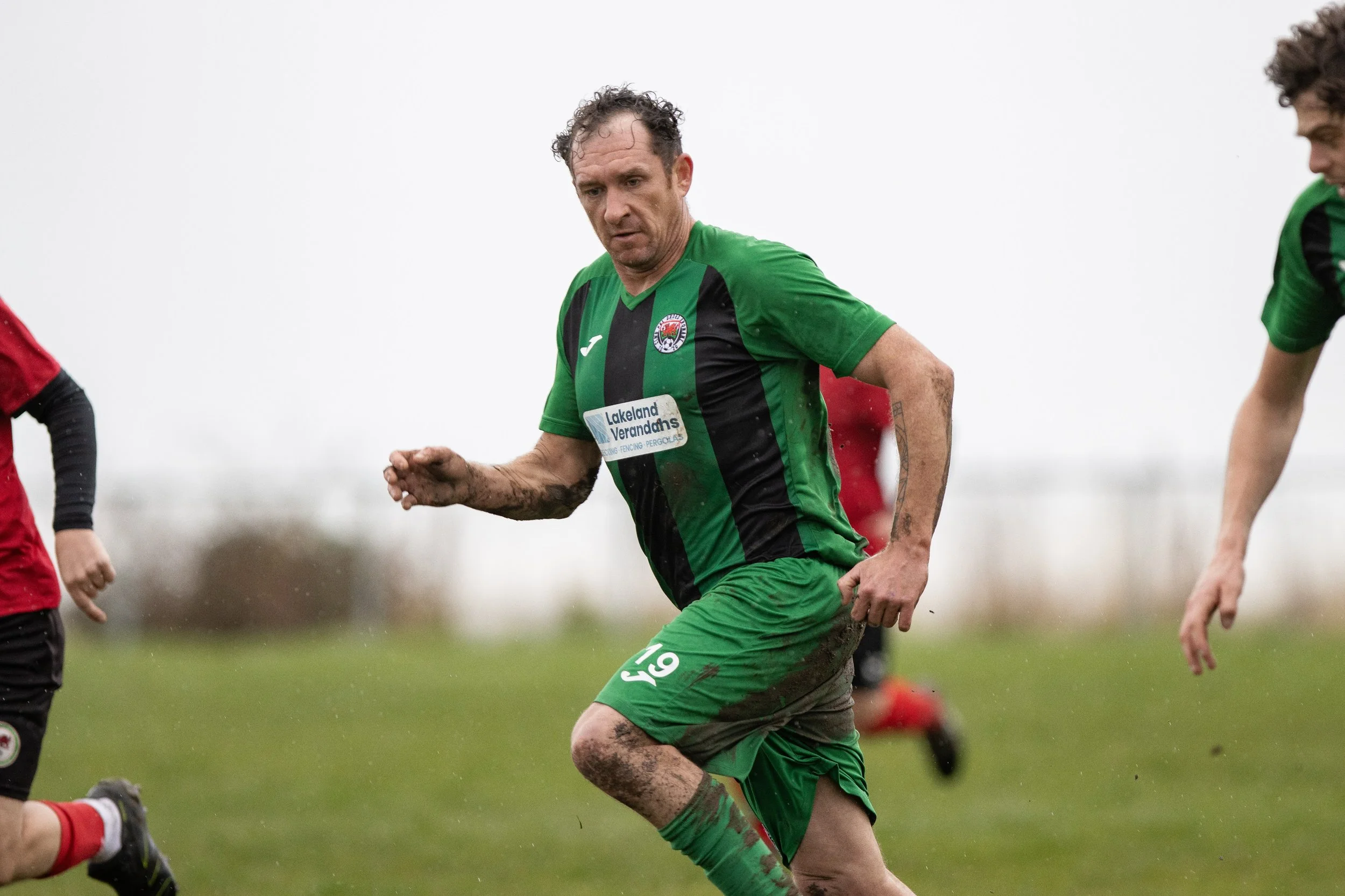 A soccer player wearing a green and black uniform running on a muddy field.