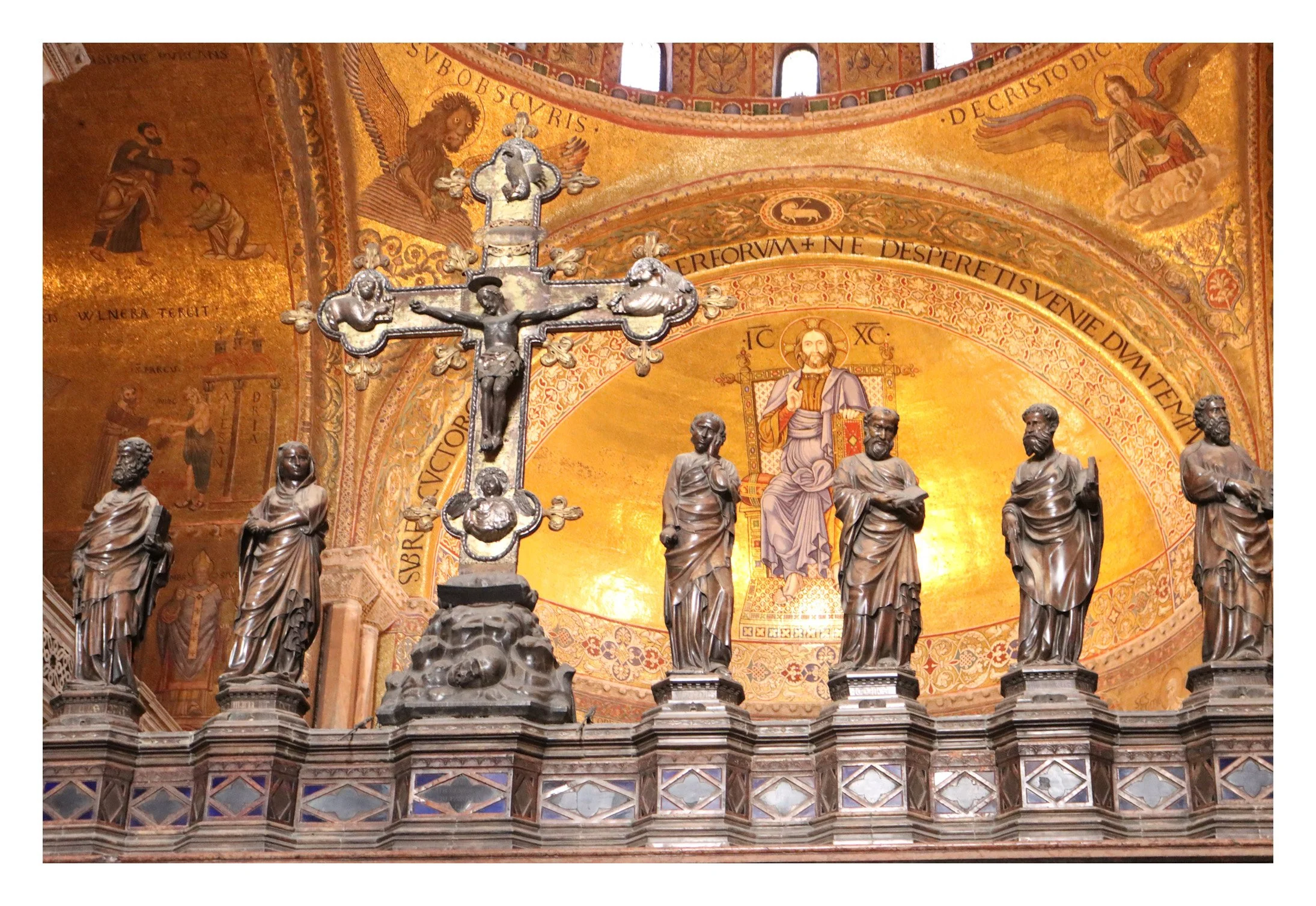 Church altar with a crucifix and seven statues of saints against a gold mosaic background.