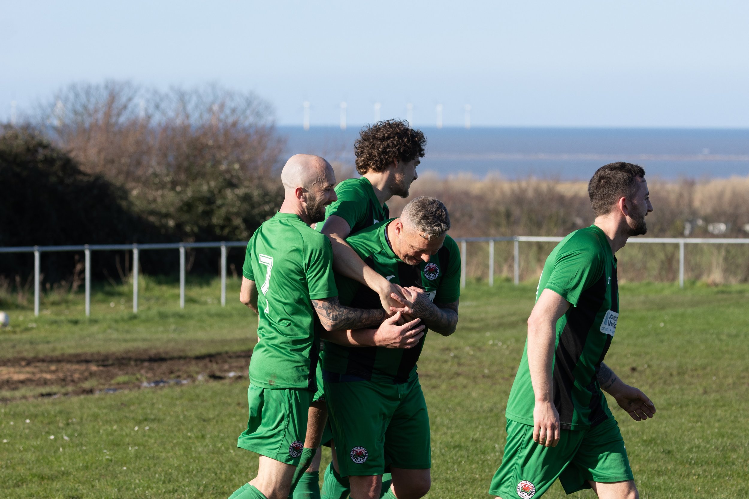 Four soccer players in green jerseys celebrating on the field.
