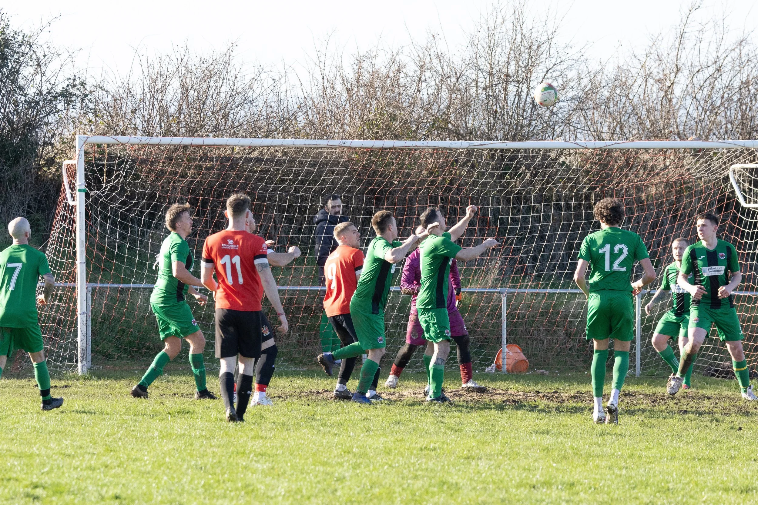 Soccer match with players in green and red uniforms near the goal, attempting to head the ball.
