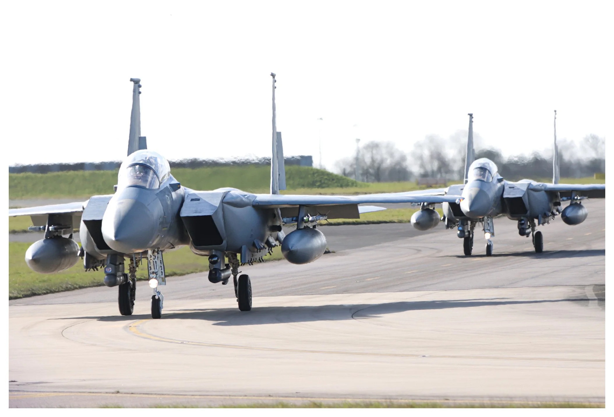 Two F-15 fighter jets taxiing on the runway at an airport.