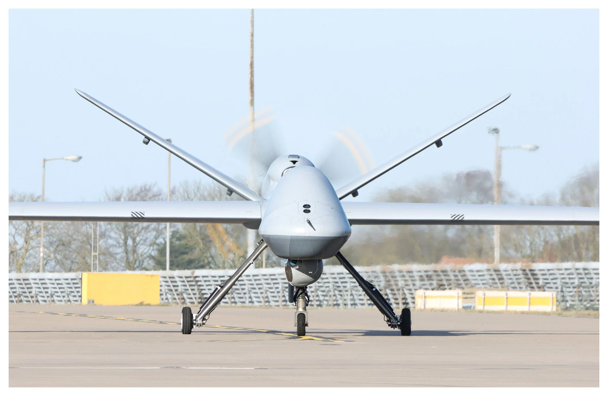 A military drone taxiing on an airport runway with its propeller spinning, viewed from the front.