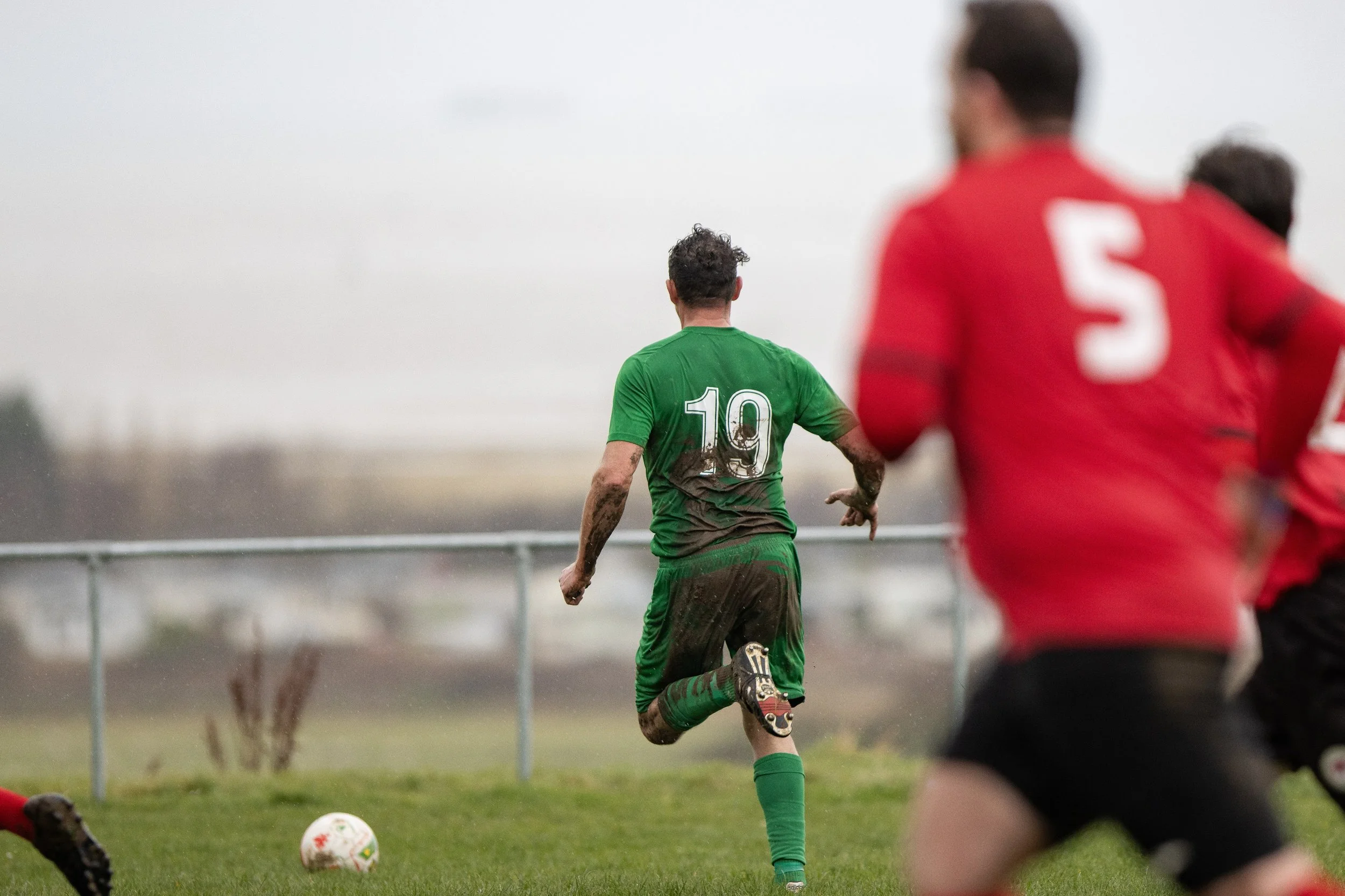 Soccer players on a field, with a player in a green uniform marked number 19, running towards the goal while others in red are pursuing him.