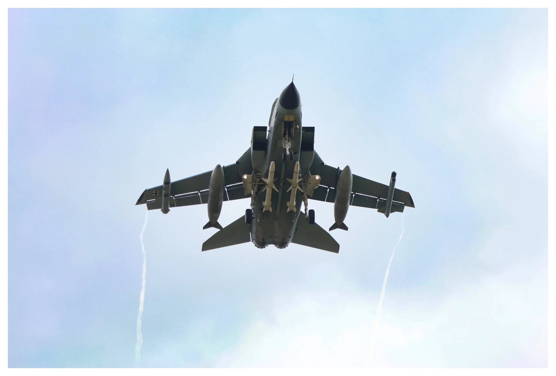 Fighter jet airplane flying in the sky with contrail streaks behind it.