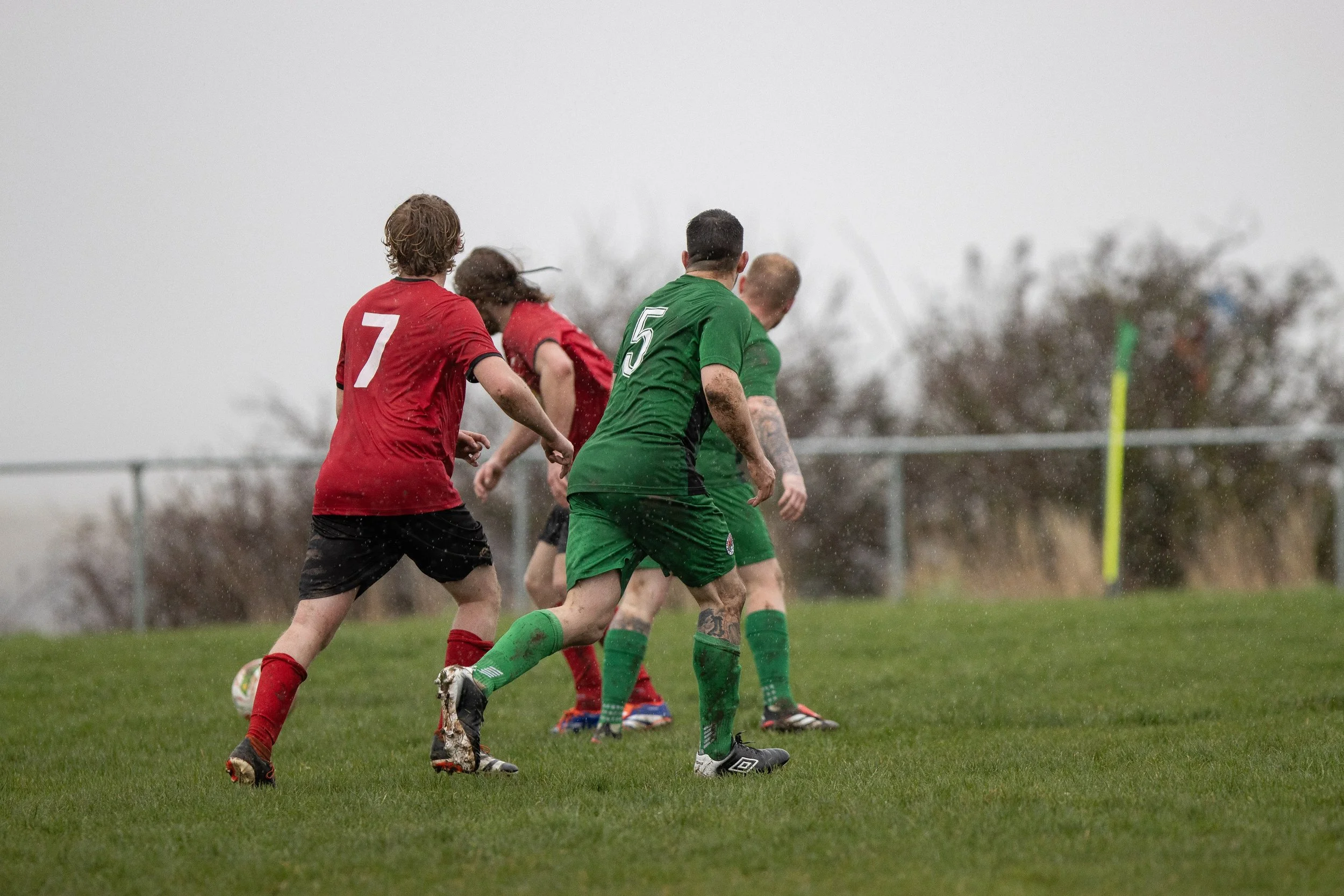 Soccer players in red and green jerseys playing on field in rainy weather.