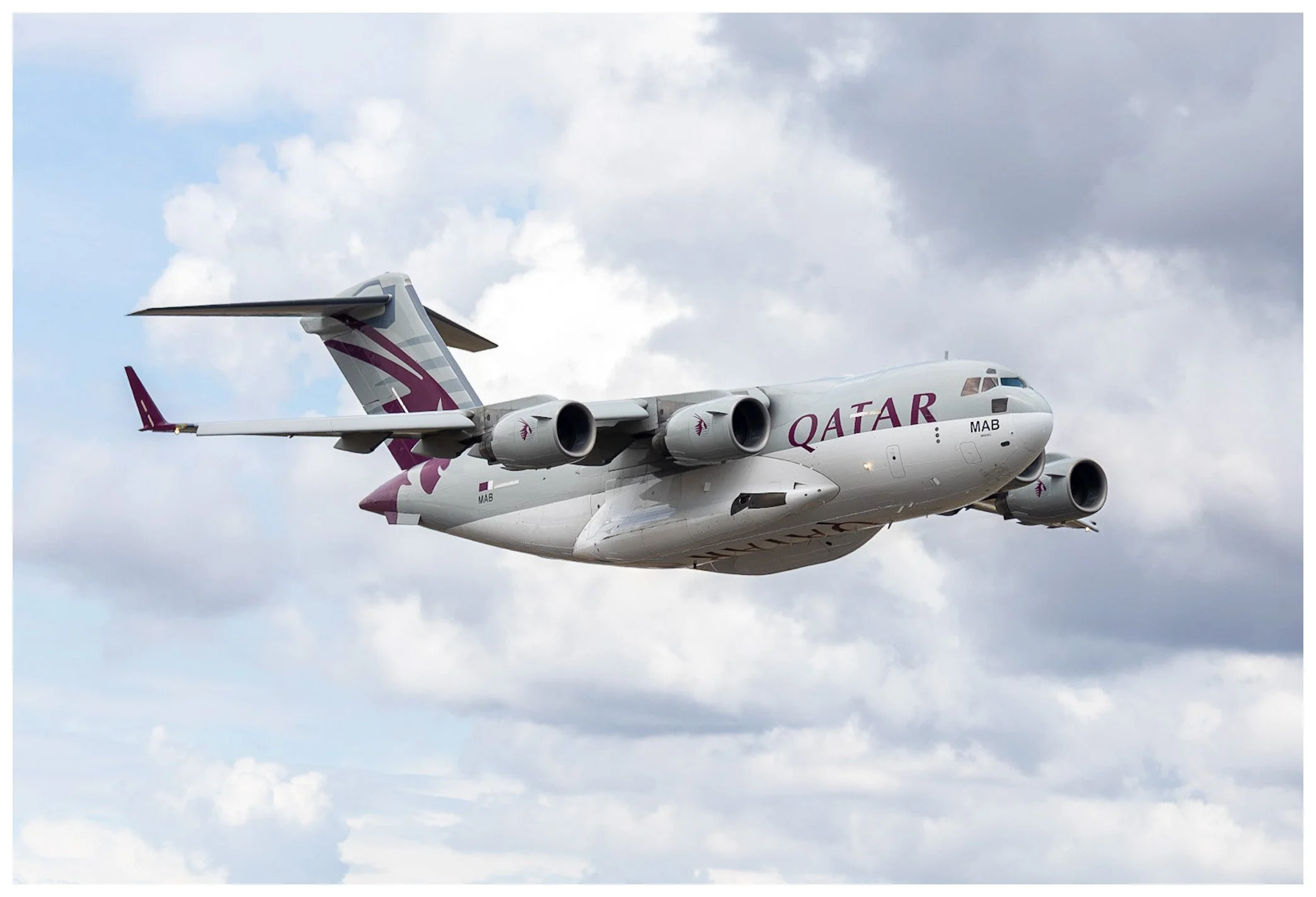 A Qatar Airways cargo airplane flying in the sky with clouds in the background.