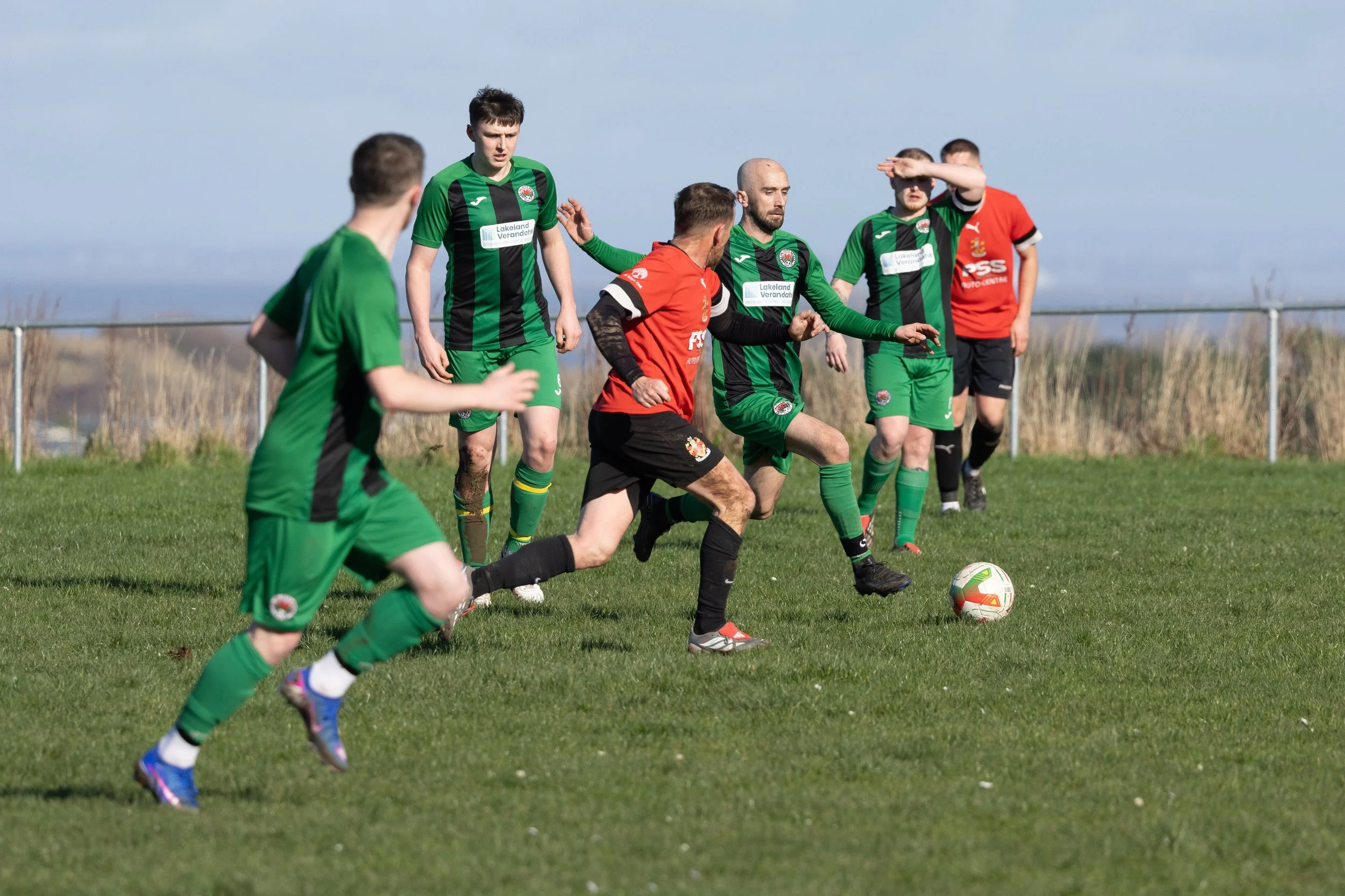 Soccer match with players in green and red uniforms competing for ball on a grassy field.