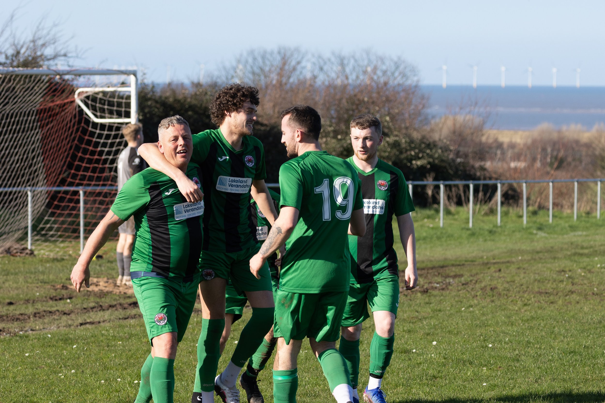 Soccer players in green and black uniforms celebrating on the field.