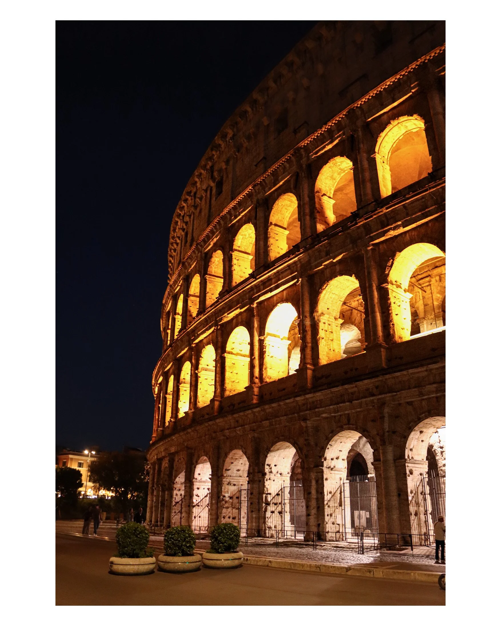 The illuminated exterior of the Colosseum at night in Rome, Italy, showcasing its arches and ancient stone structure.
