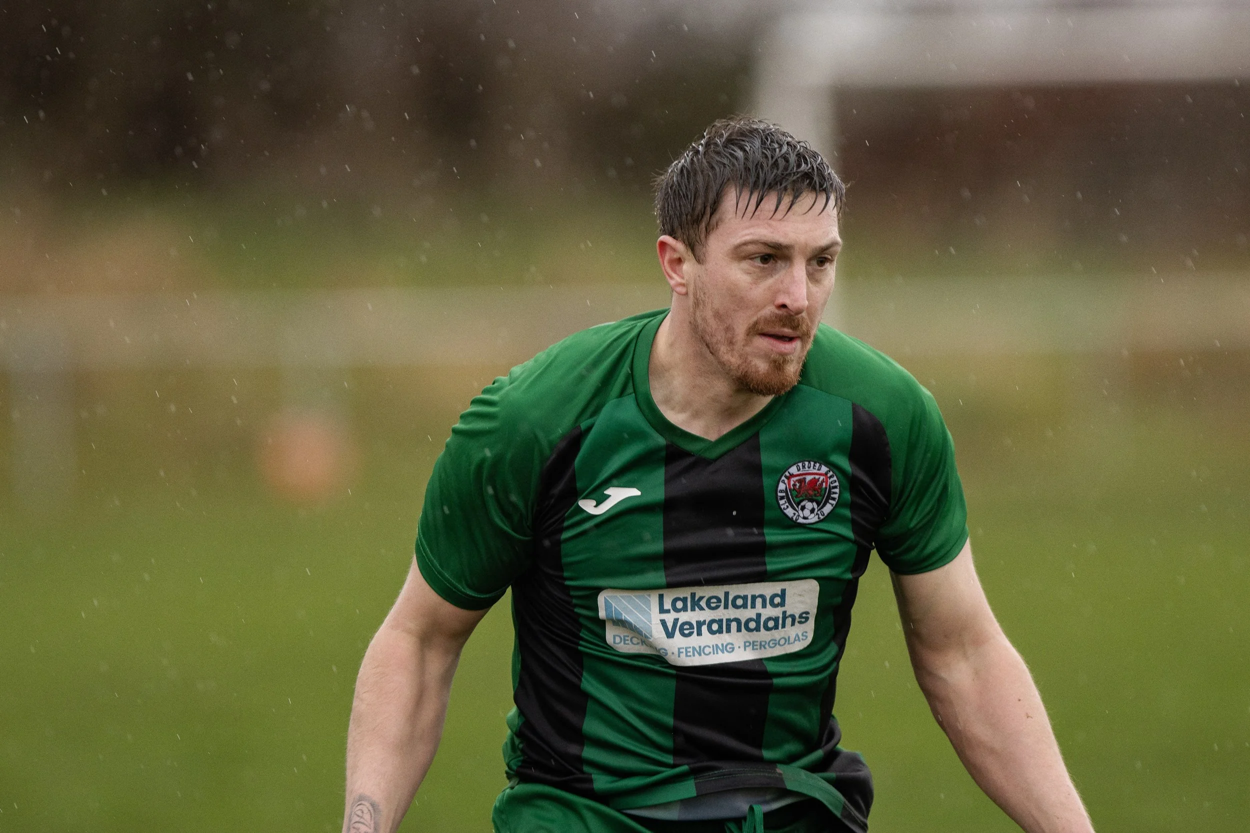 A male soccer player in a green and black jersey on the field in the rain.