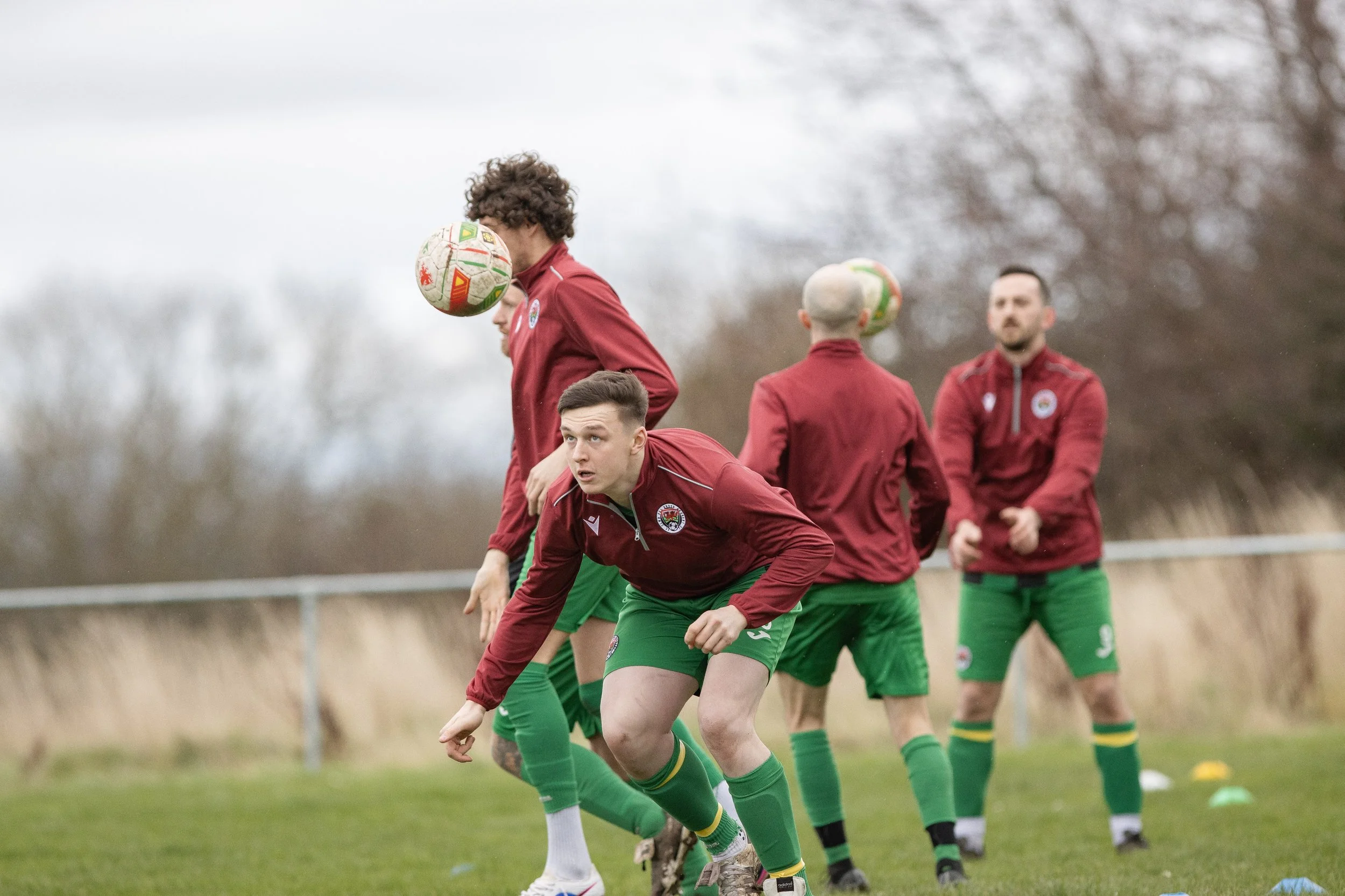 Soccer players practicing on a field outdoors, wearing red jerseys and green shorts.