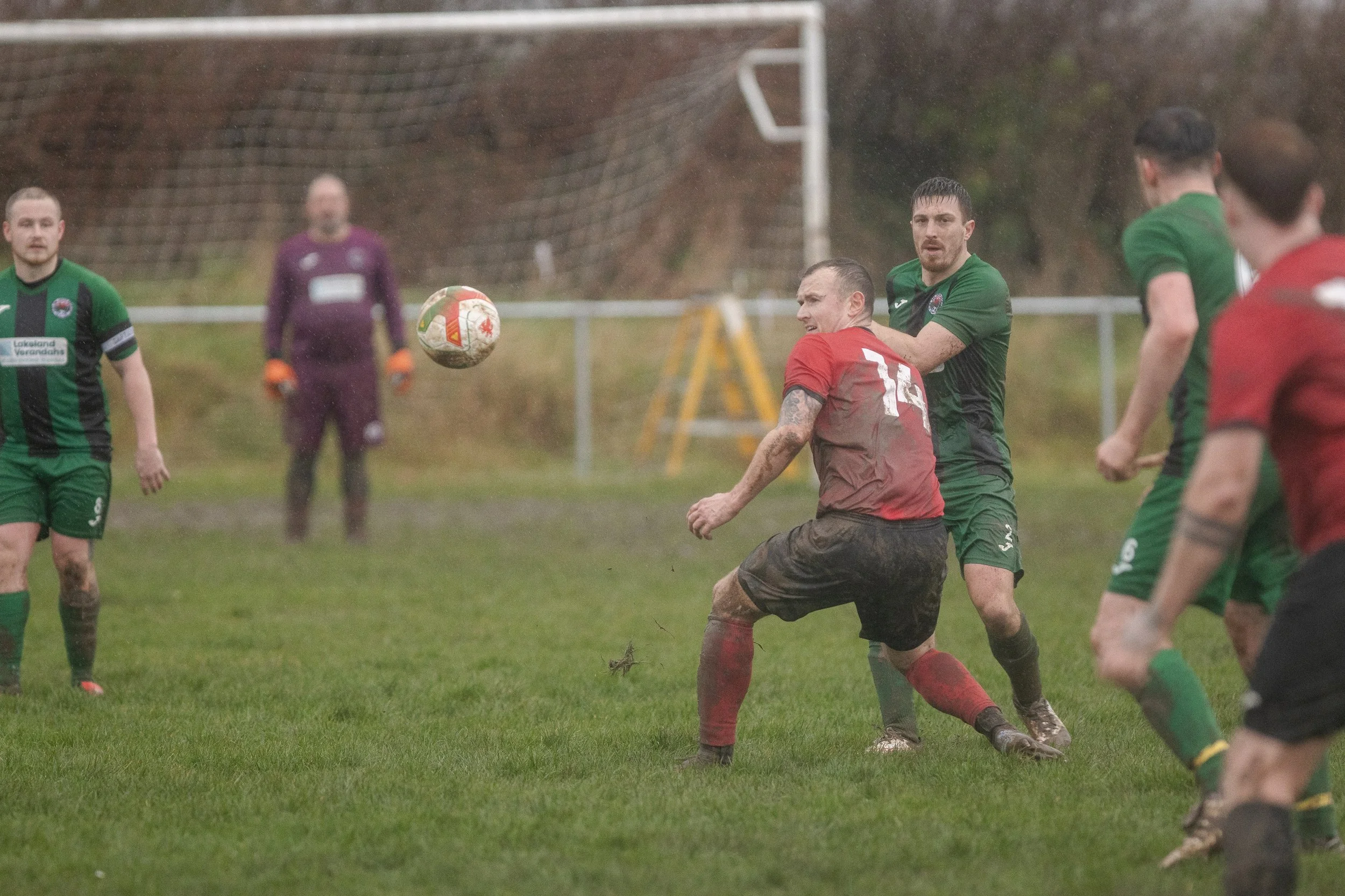 Soccer players competing for the ball on a muddy field during a match in rainy weather.