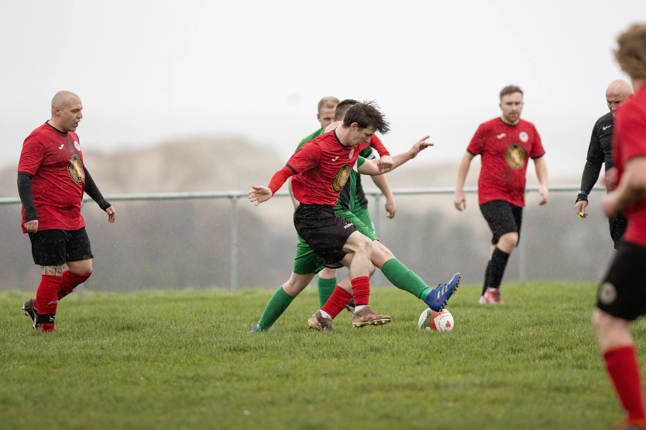 Soccer players in red and green jerseys competing for ball on rainy field.