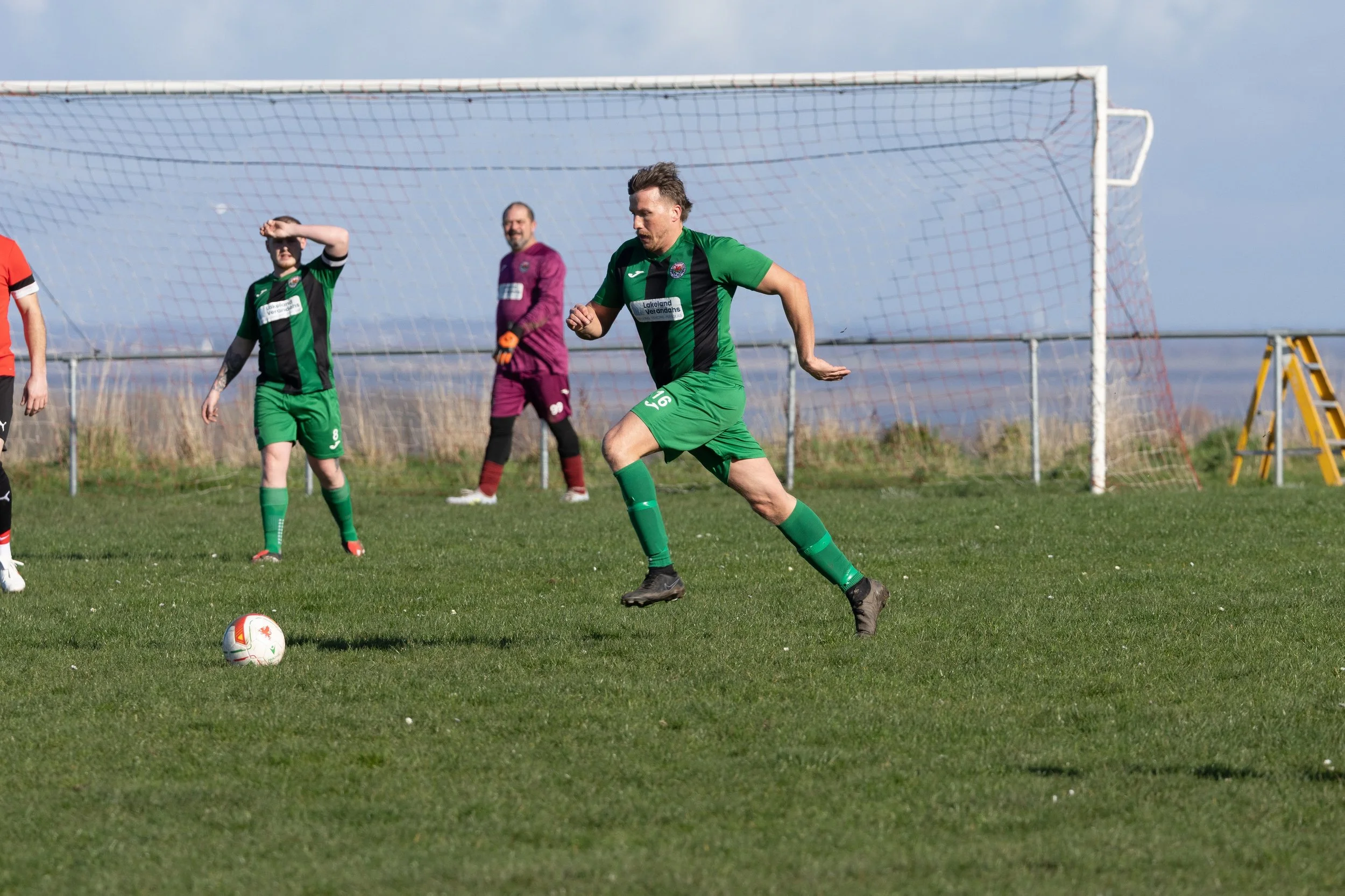 Soccer players in green uniforms playing on a grassy field near a goal post.