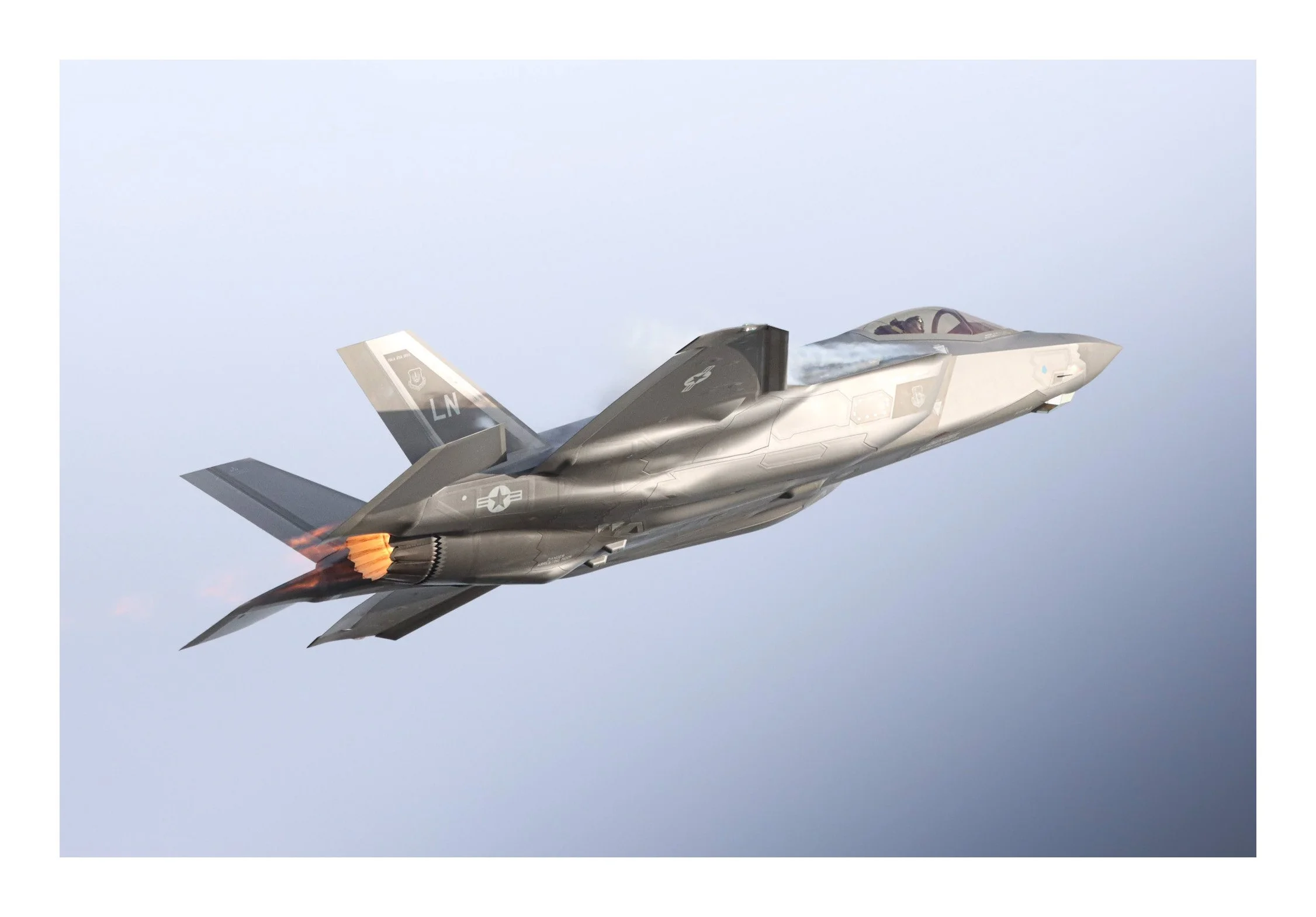 A fighter jet in flight with afterburner flames visible, against a cloudy sky background.