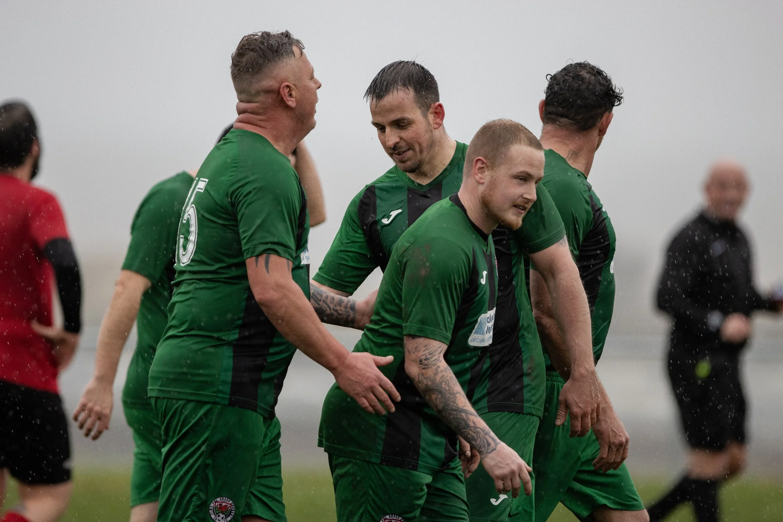 Soccer players in green jerseys celebrating on the field during a rainy match.
