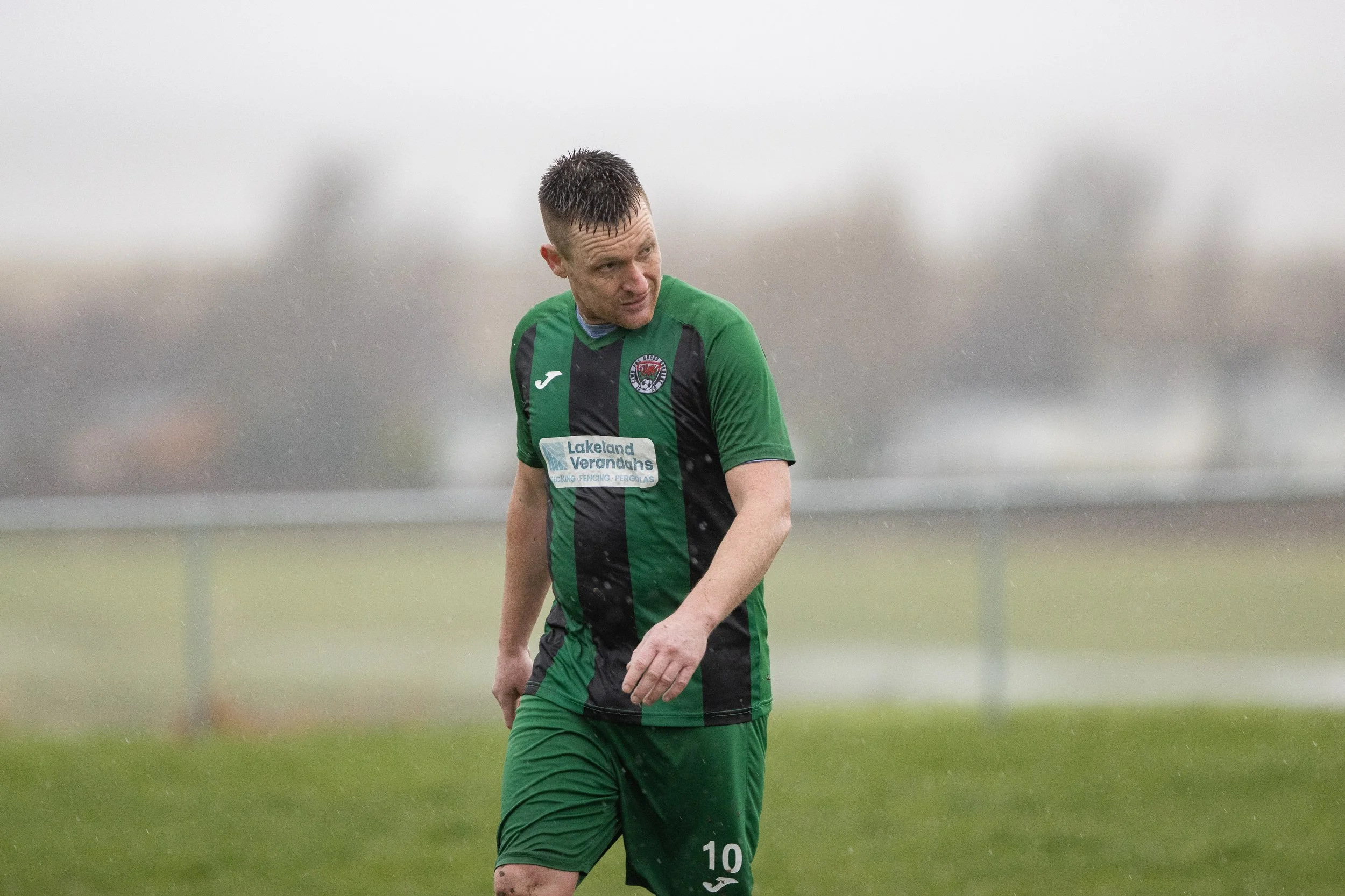 Soccer player in a green and black uniform walking on a rainy field.
