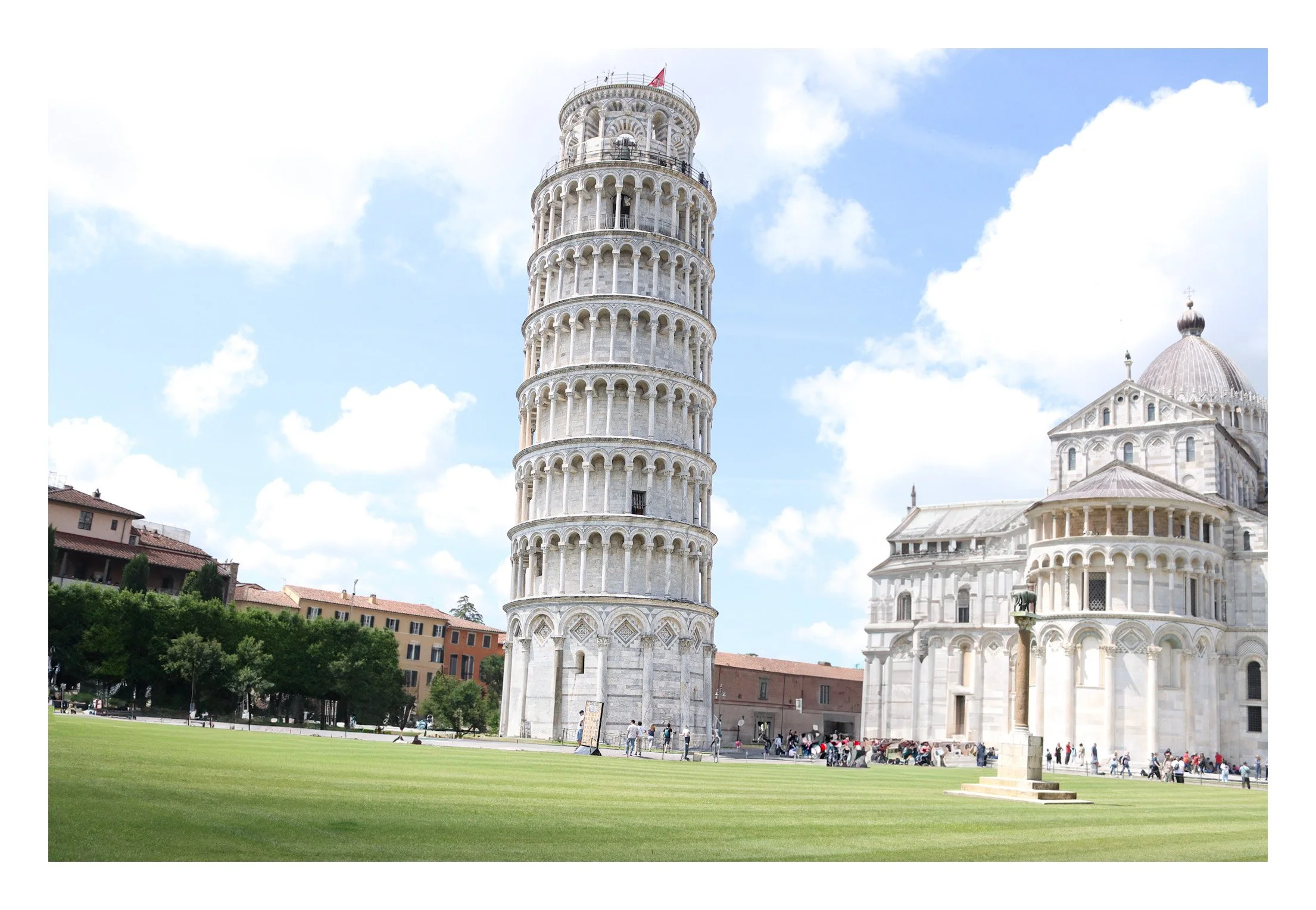 Pisa Tower in Italy with a green lawn in the foreground and a church with a dome to the right, under a partly cloudy sky.